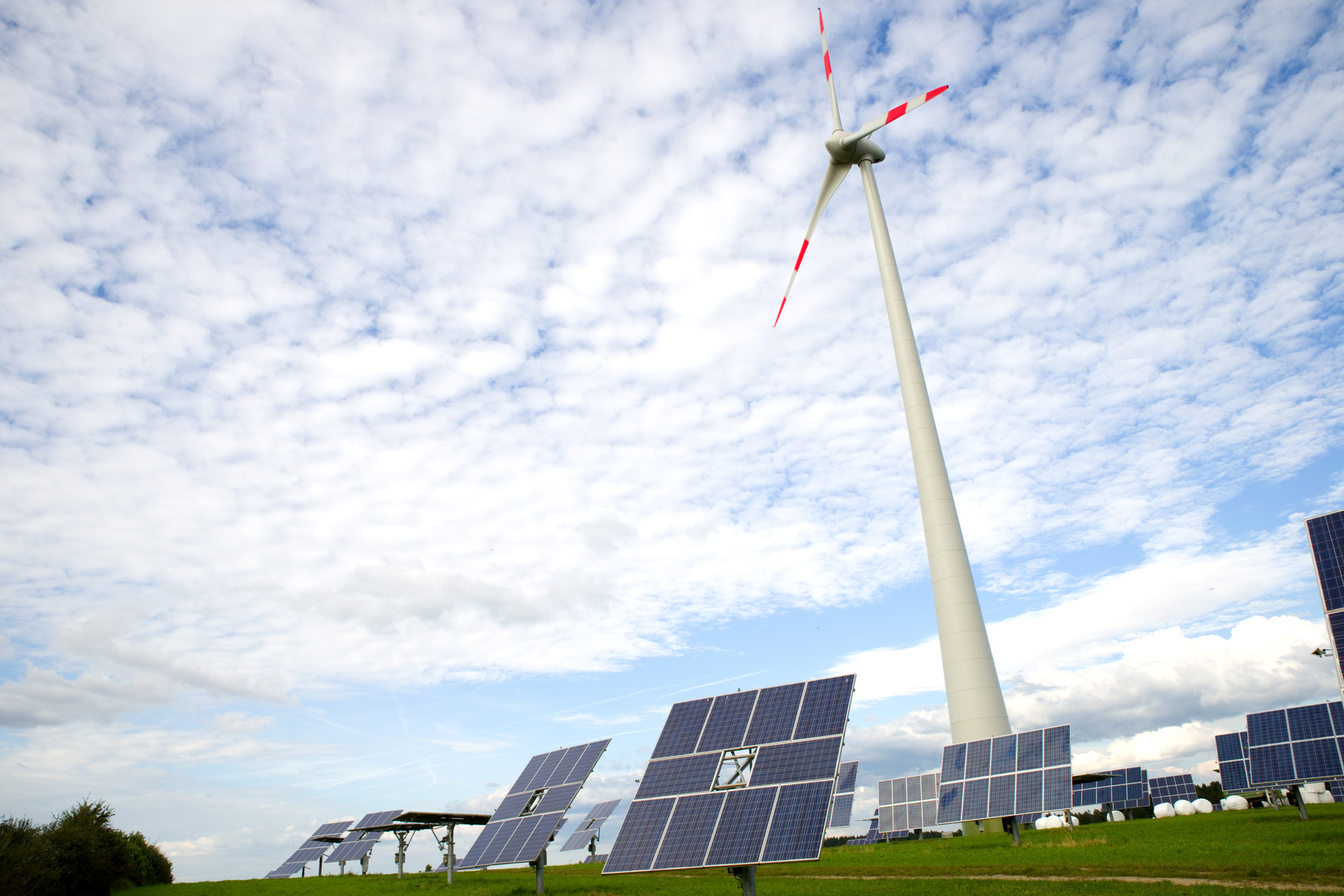 Photovoltaik- und Windenergieanlagen vor blauem Himmel mit Schäfchenwolken.