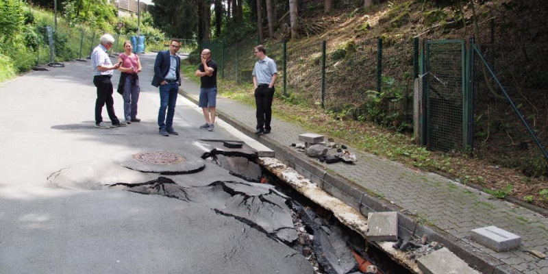 Fünf Personen begutachten eine durch eine Sturzflut geschädigte Straße