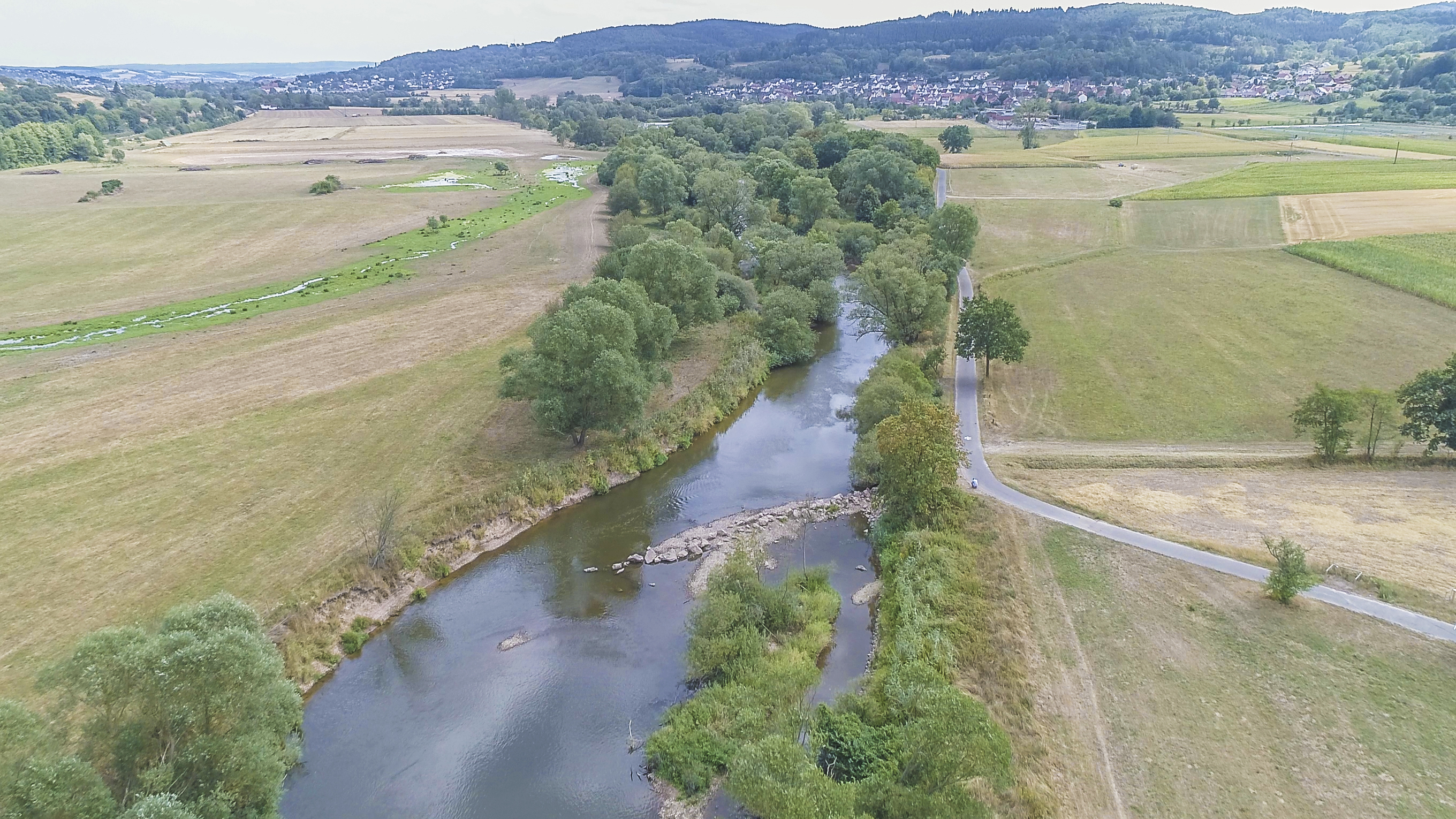 Luftbild der Fulda mit schräg zur Fließrichtung eingebrachten Steinen. Die dadurch abgelenkte Strömung hat bereits eine Erosion des Ufers bewirkt.