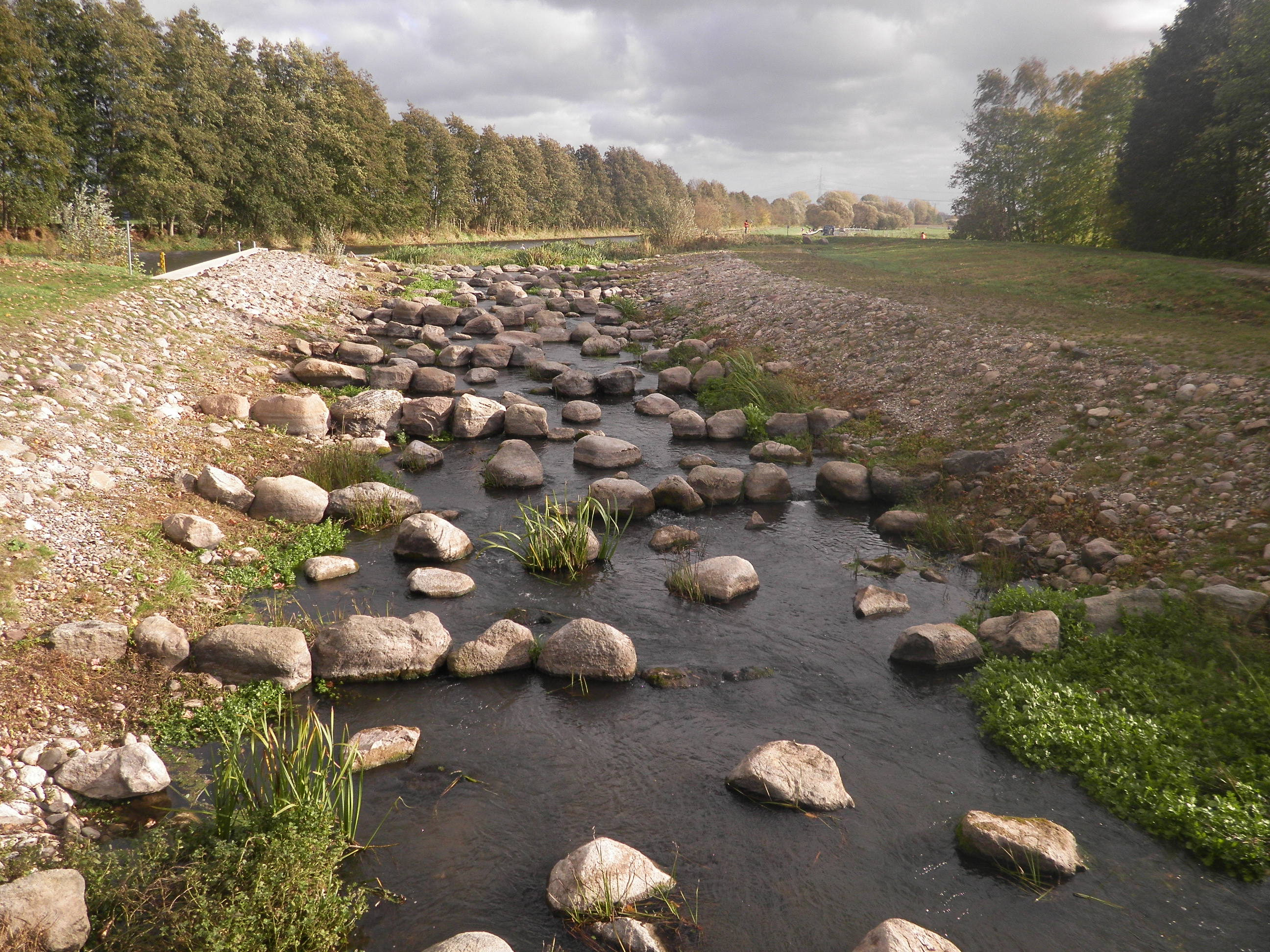 Foto: Die fertiggestellte Fischaufstiegsanlage in Lüssow. Eine langgezogene Gleite mit vielen größeren Steinblöcke im Gewässer ersetzt das alte Streichwehr.