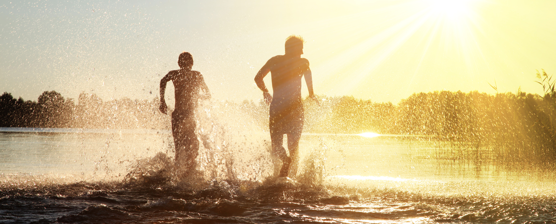 Zwei Menschen rennen freudig ins Wasser.