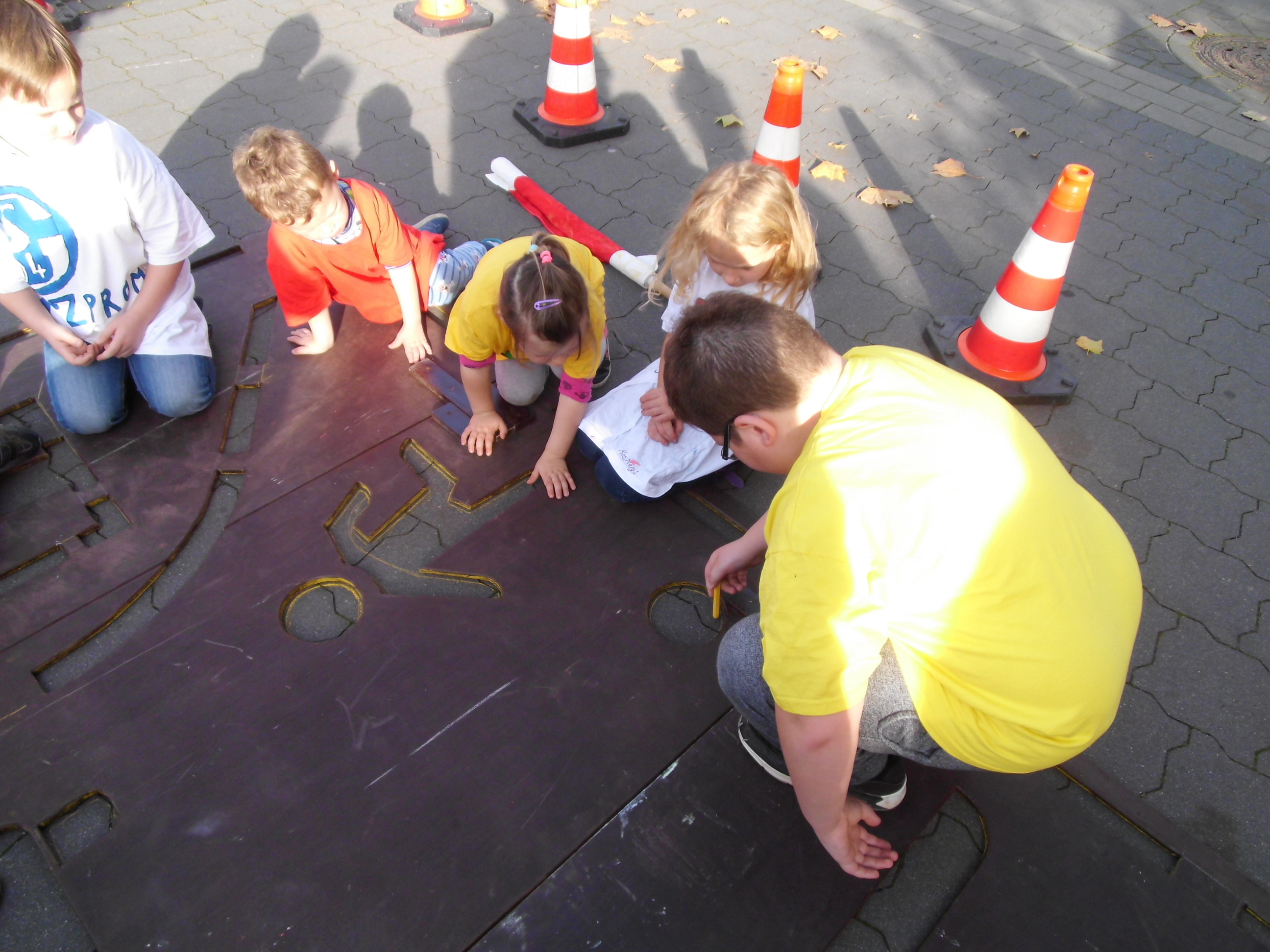Kinder zeichnen die Umrisse des Verkehrsschilds auf den Boden