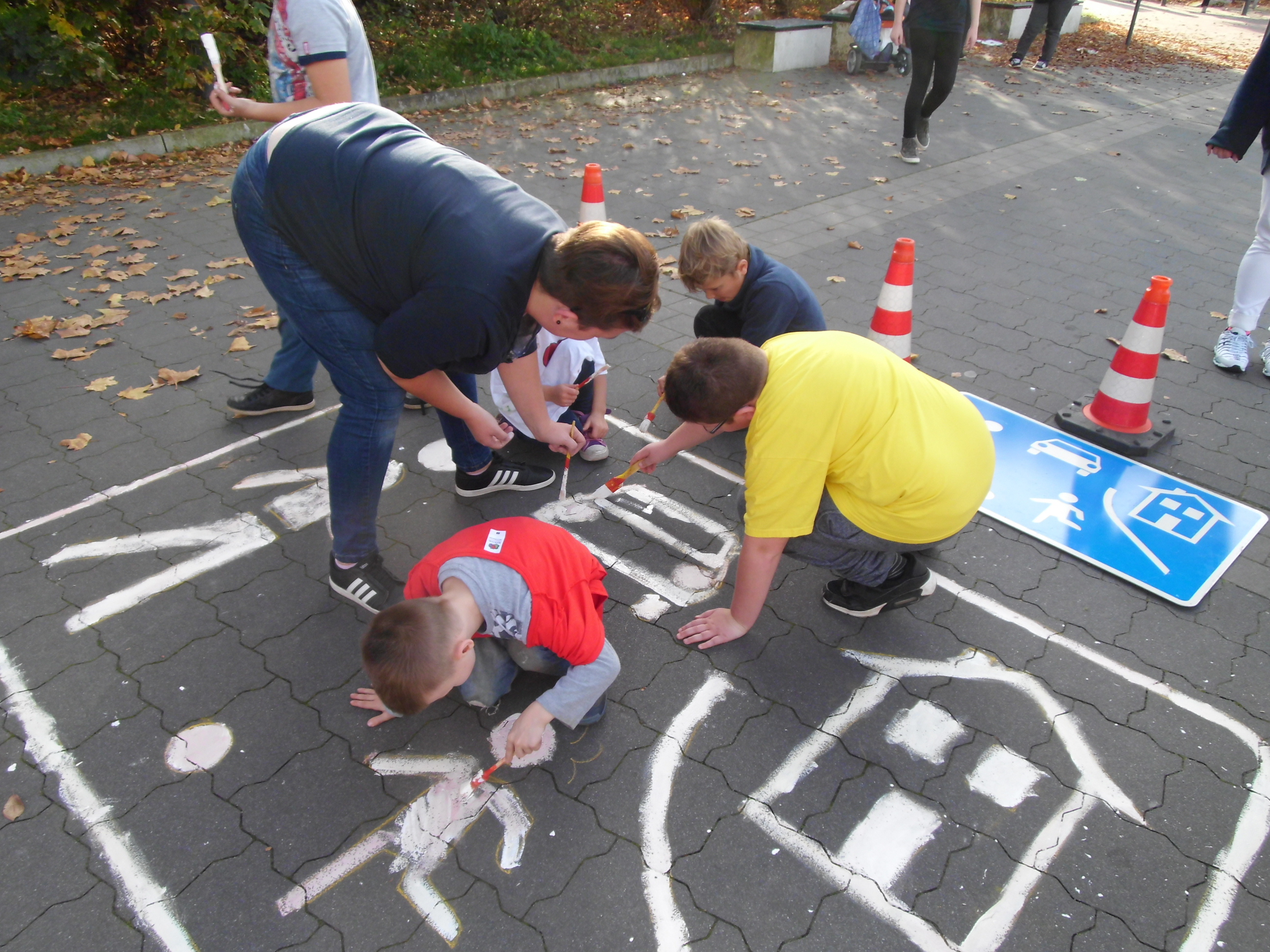 Eltern und Kinder malen das Straßenschild "verkehrsberuhigter Bereich" auf den Asphalt