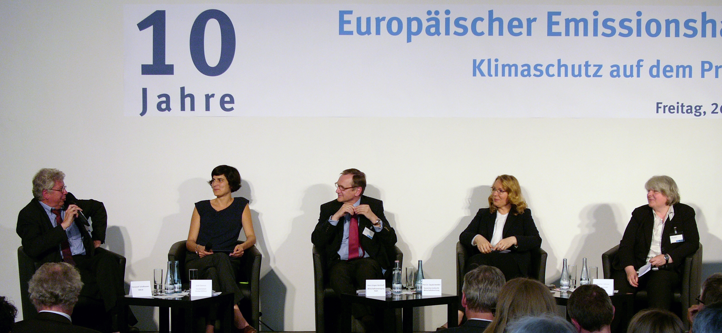 drei Frauen und zwei Männer sitzen auf einem Podium und diskutieren. Auf einem Banner darüber steht "10 Jahre Europäischer Emissionshandel"