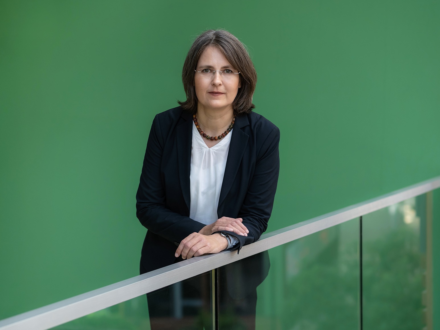 Dr. Claudia Röhl leaning on a stair railing in front of green background