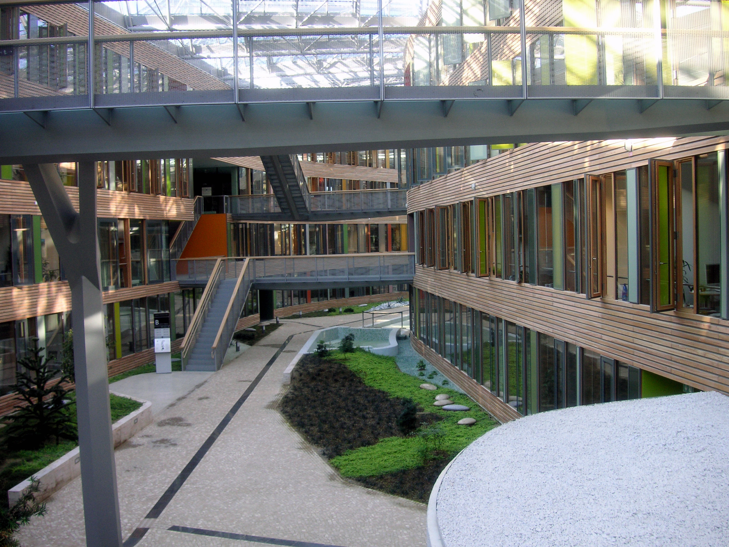 langgestreckter Innenhof mit Glasdach, Verbindungsbrücken zwischen dem linken und rechten Gebäudeteil, Anpflanzungen und Wasserbecken