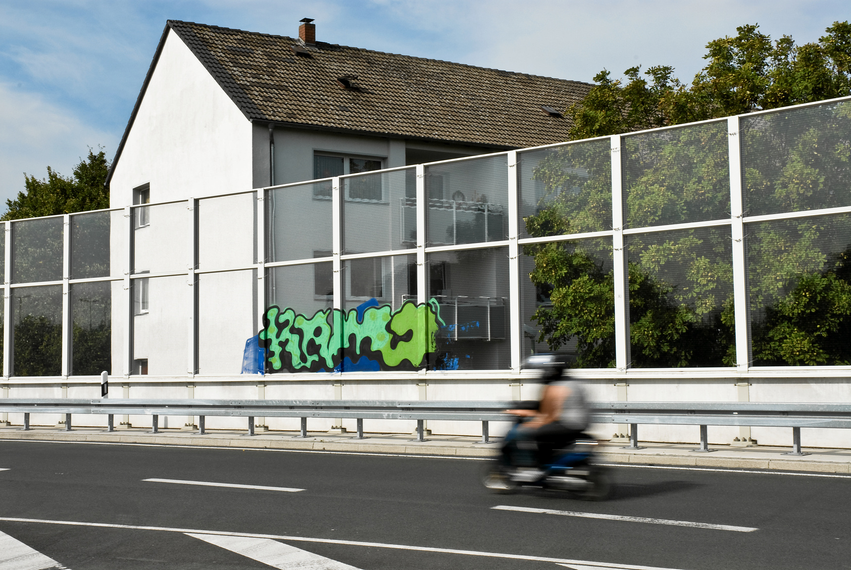 ein mehrstöckiges Wohnhaus mit Balkonen steht direkt hinter einer Lärmschutzwand einer Stadtautobahn
