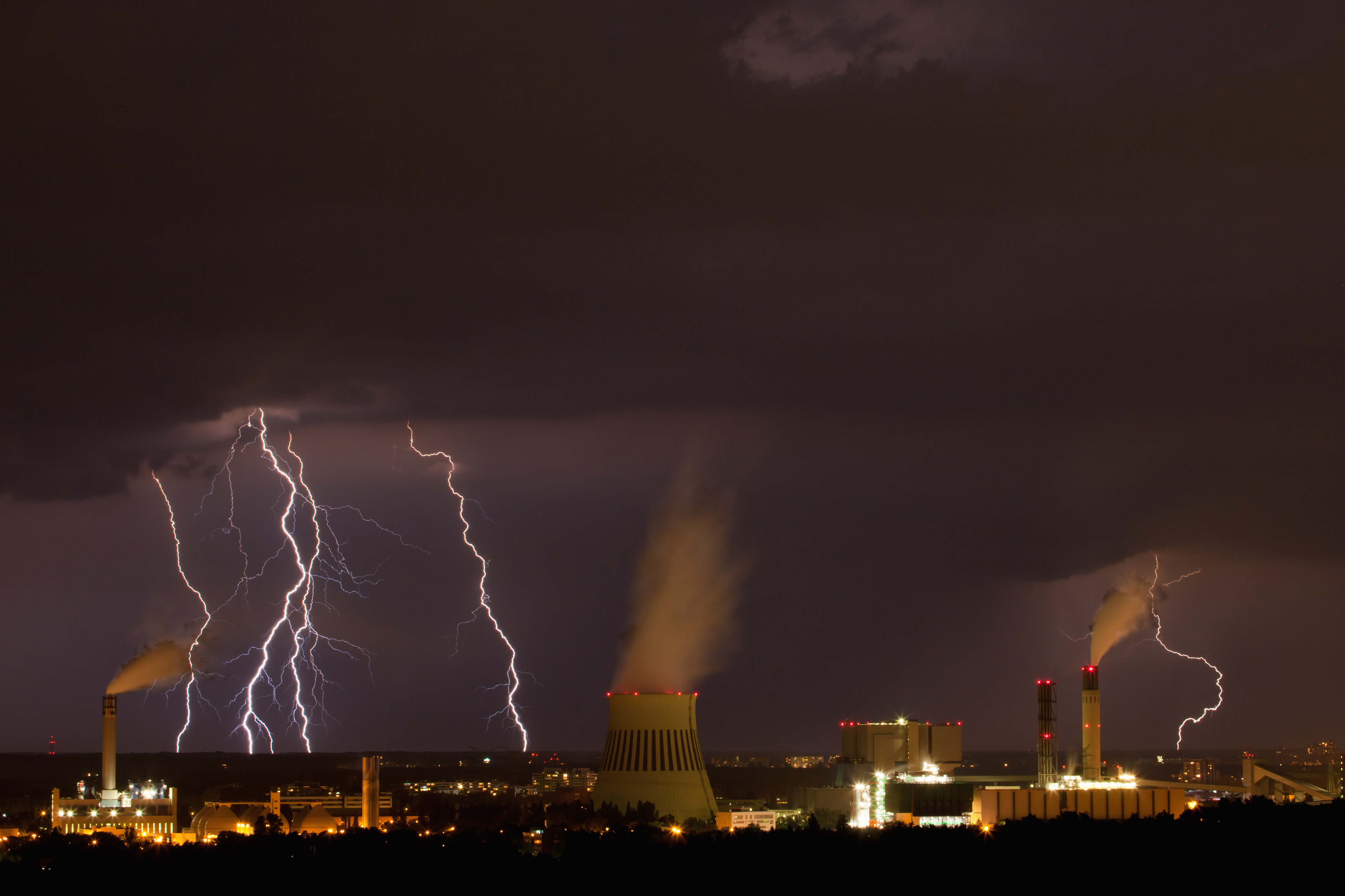 über einer Industrieanlage bei Nacht tobt ein Unwetter mit Blitzen und dunklen Wolken