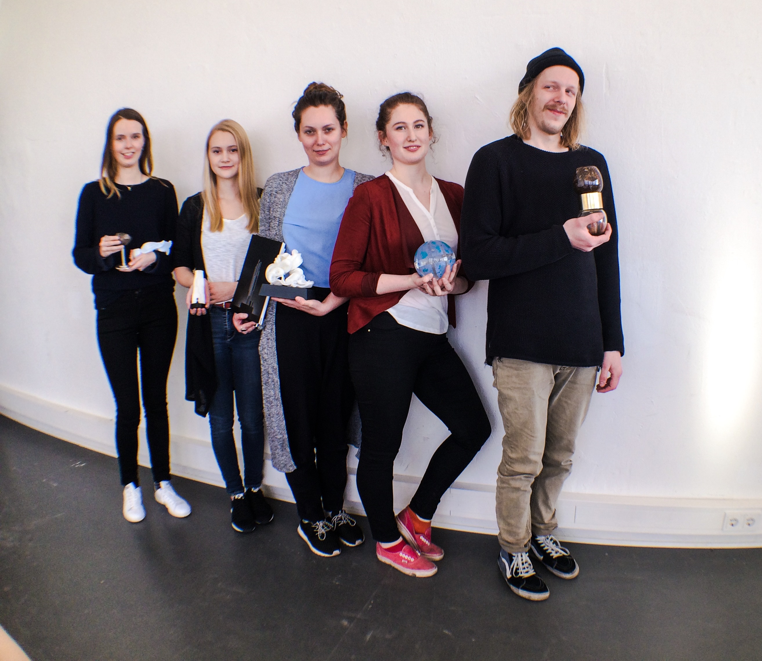 vier junge Frauen und ein junger Mann mit Trophäen in der Hand an eine Wand gelehnt