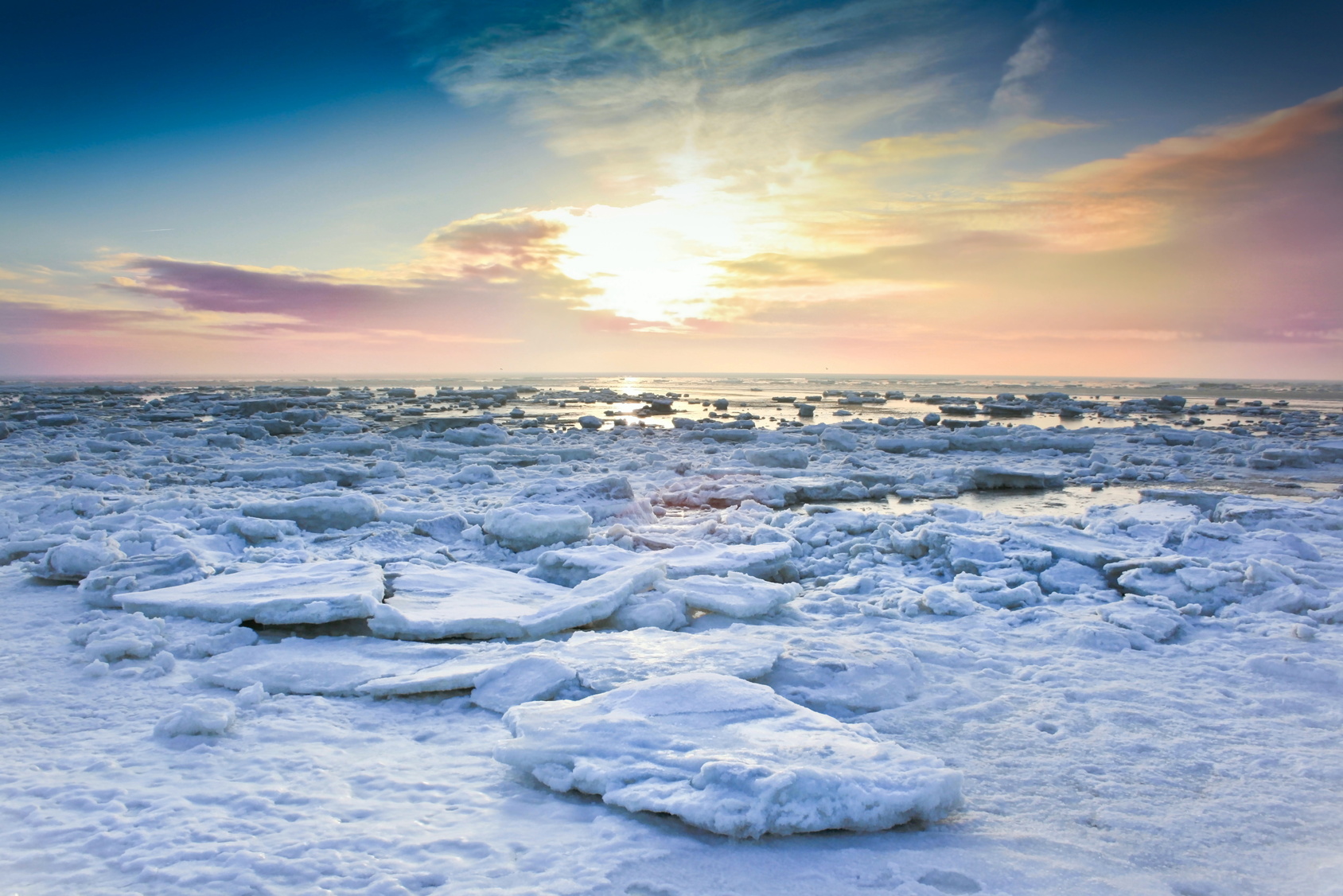 Eisschollen auf dem Meer, im Hintergrund färbt die tief stehende Sonne die Wolken am Horizont rosa