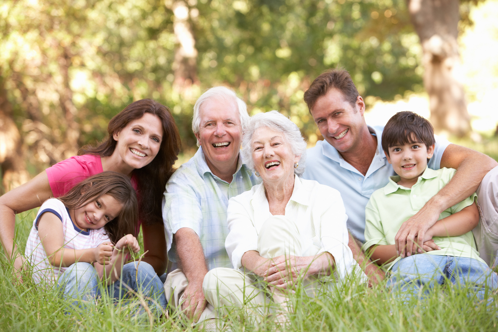 Girl and boy, their parents and grandparents are sitting on a lawn in a park.