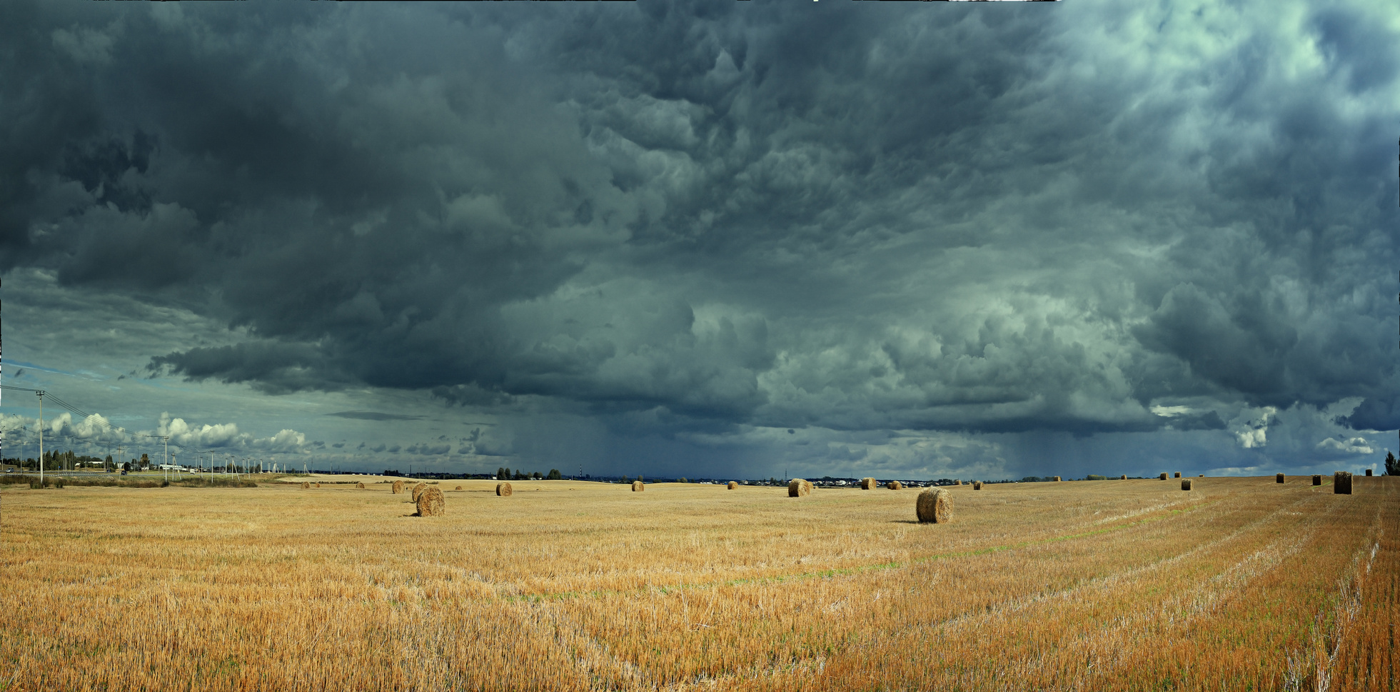 abgeerntetes Getreidefeld mit gelben Stoppeln und Strohballen. Am Himmel türmen sich bedrohlich dunkle und niedrig hängende Wolken.