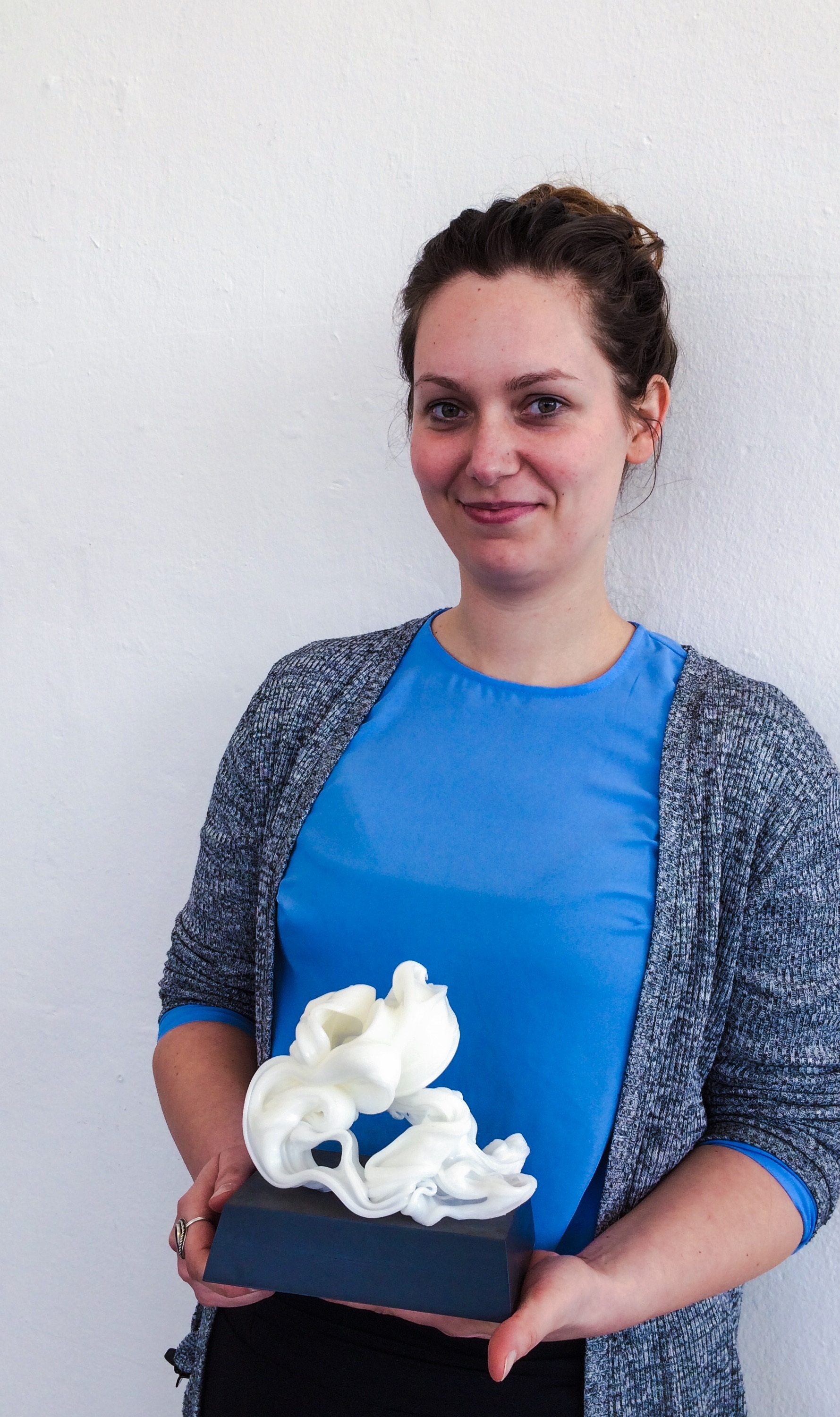 junge Frau mit einer Trophäe in der Hand, ein weißes, filigranes Gebilde auf einem Sockel