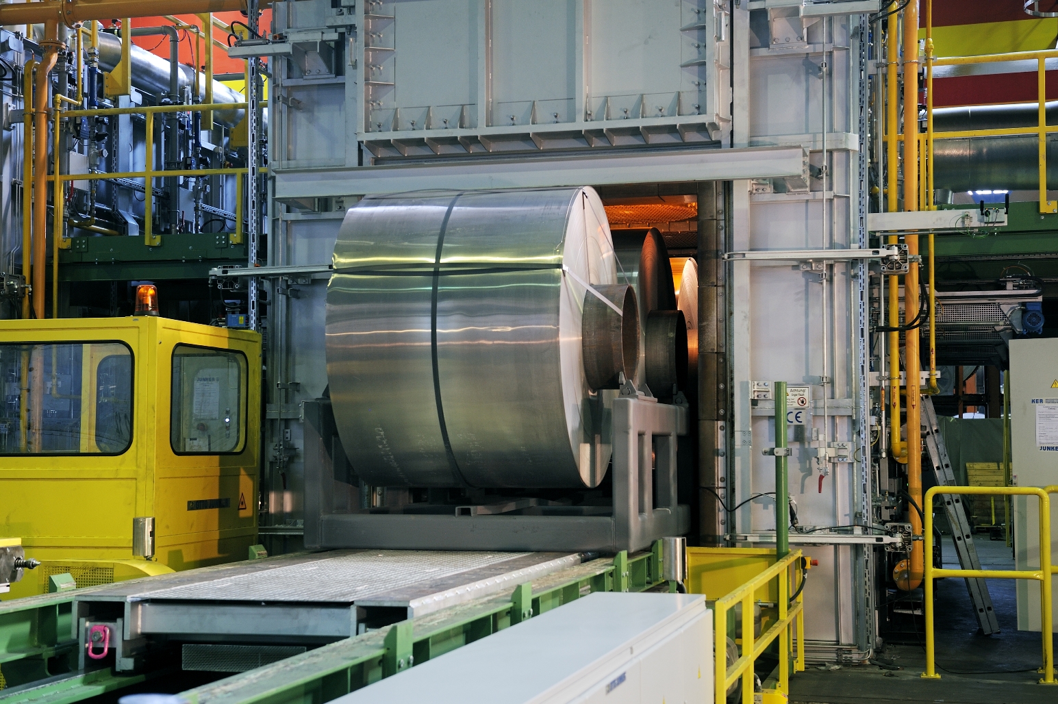 in einer Fabrikhalle wird ein große Rolle aufgerolltes Aluminiumband auf einem Förderband in eine Kammer gefahren, in der es glüht