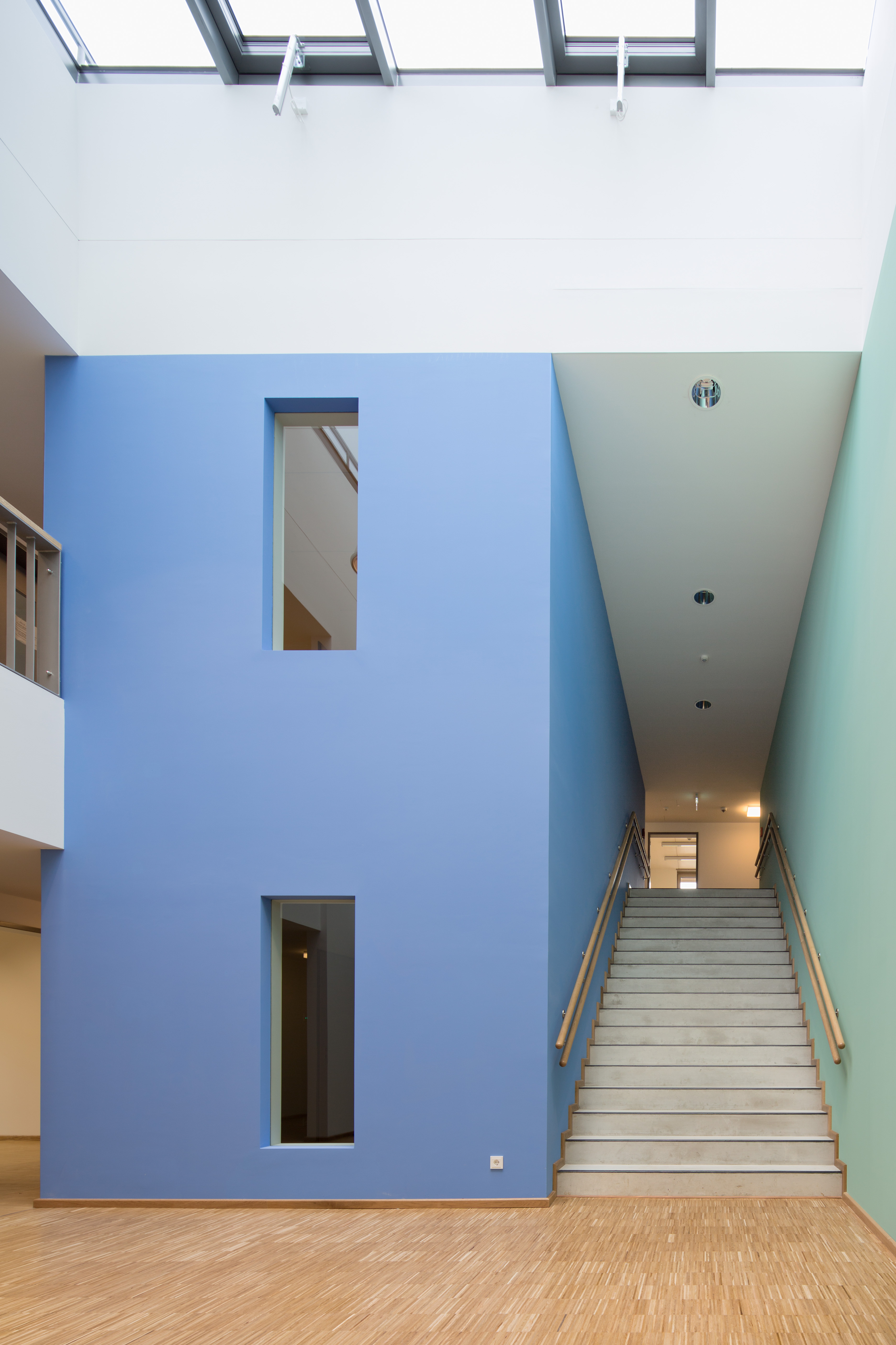 kleine Eingangshalle mit Glasdach und Treppenaufstieg, die Wände sind weiß, die Wände des Treppenhauses jedoch links blau uns rechts hellgrün gestrichen