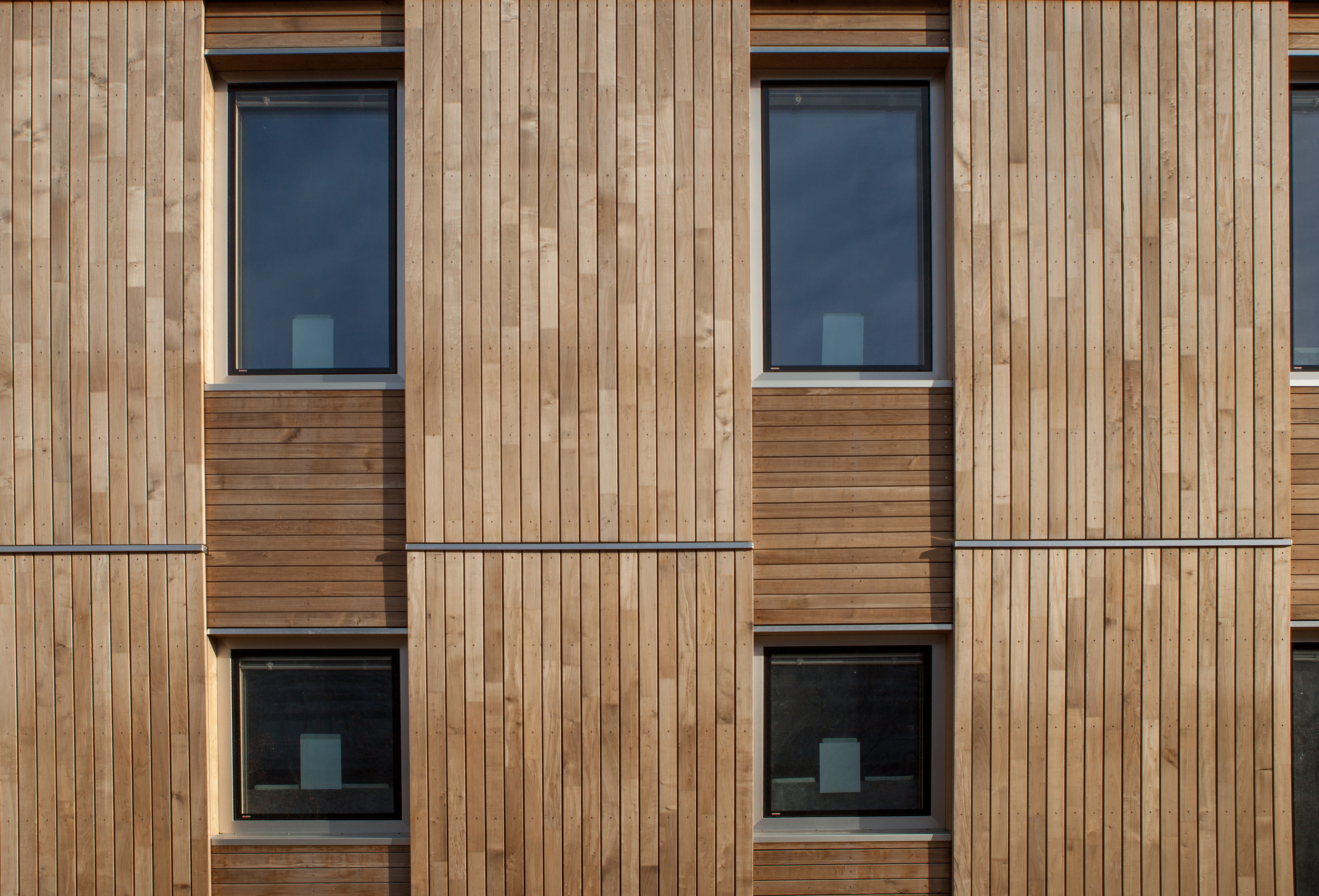 Fassade mit Holztafeln verkleidet, die Holztafeln bilden ein Raster aus größeren senkrechten Tafeln mit senkrechten Holzlatten und kleineren waagerechten Tafeln mit waagerechten Holzlatten