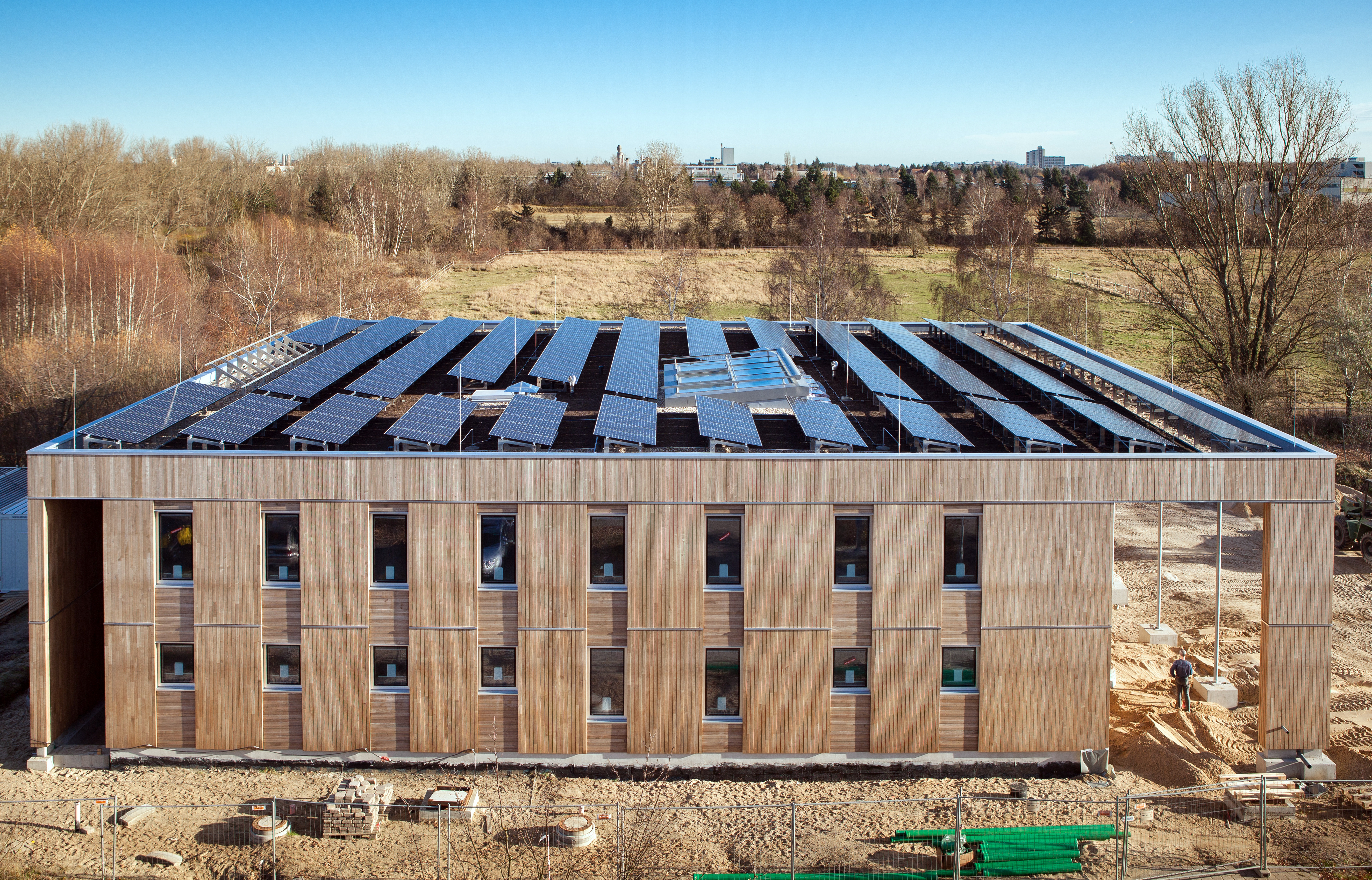 quadratischer zweigeschossiger Bau mit Holzfassade und Solarzellen auf dem Dach