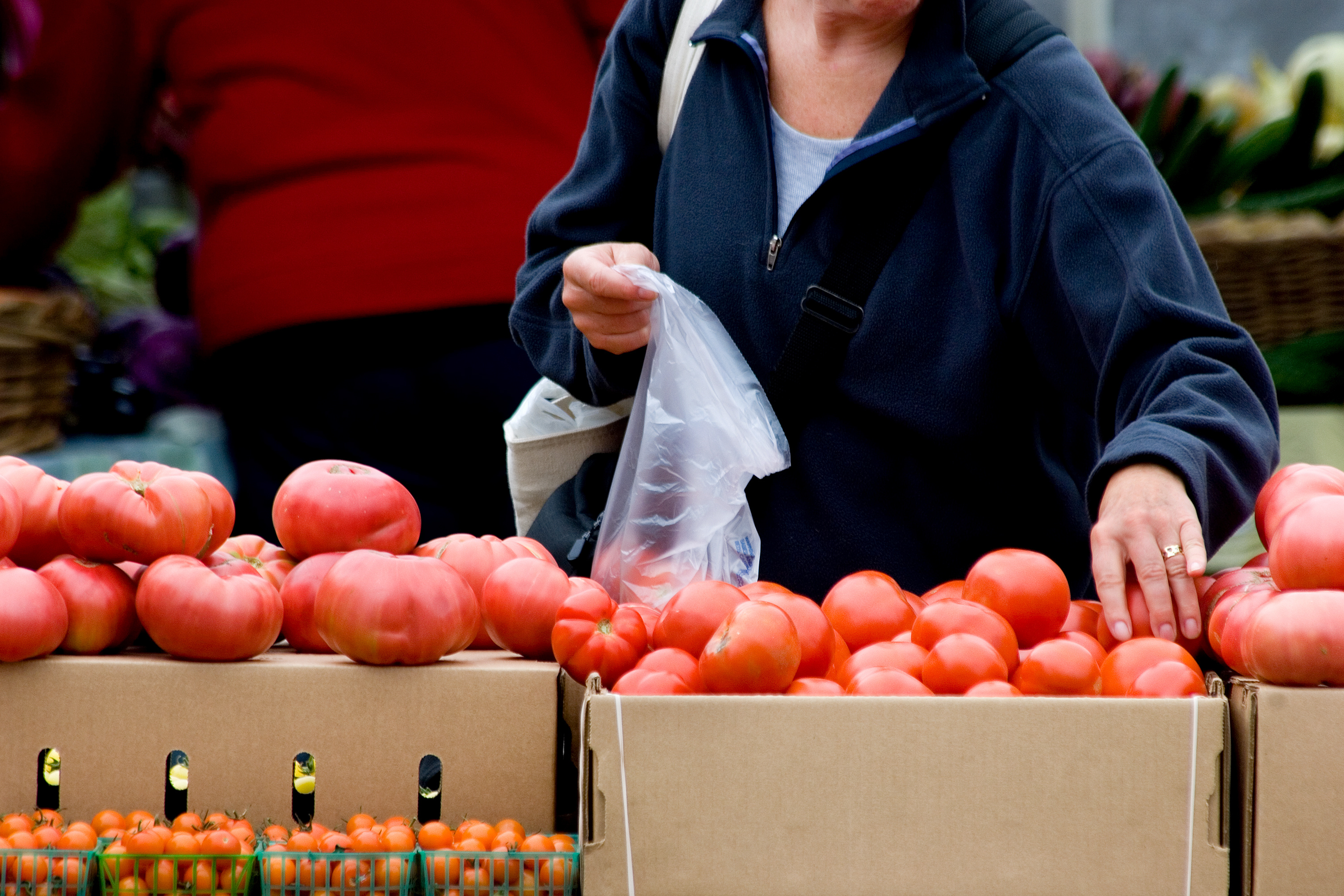 eine Kundin packt an einem Marktstand Tomaten in einen dünnen Plastikbeutel