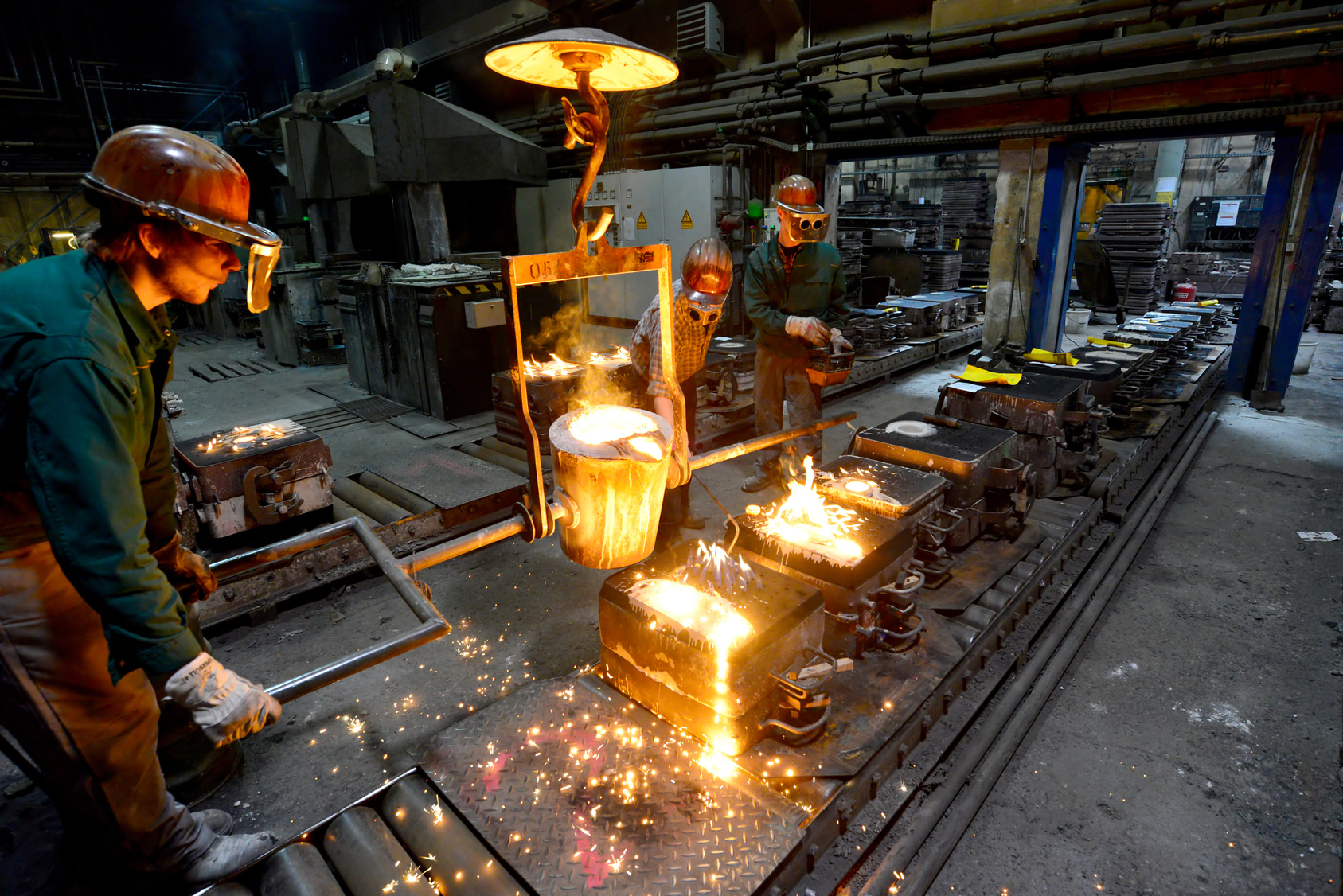 In einer Gießerei gießen Arbeiter flüssiges, glühendheißes Metall in Formen