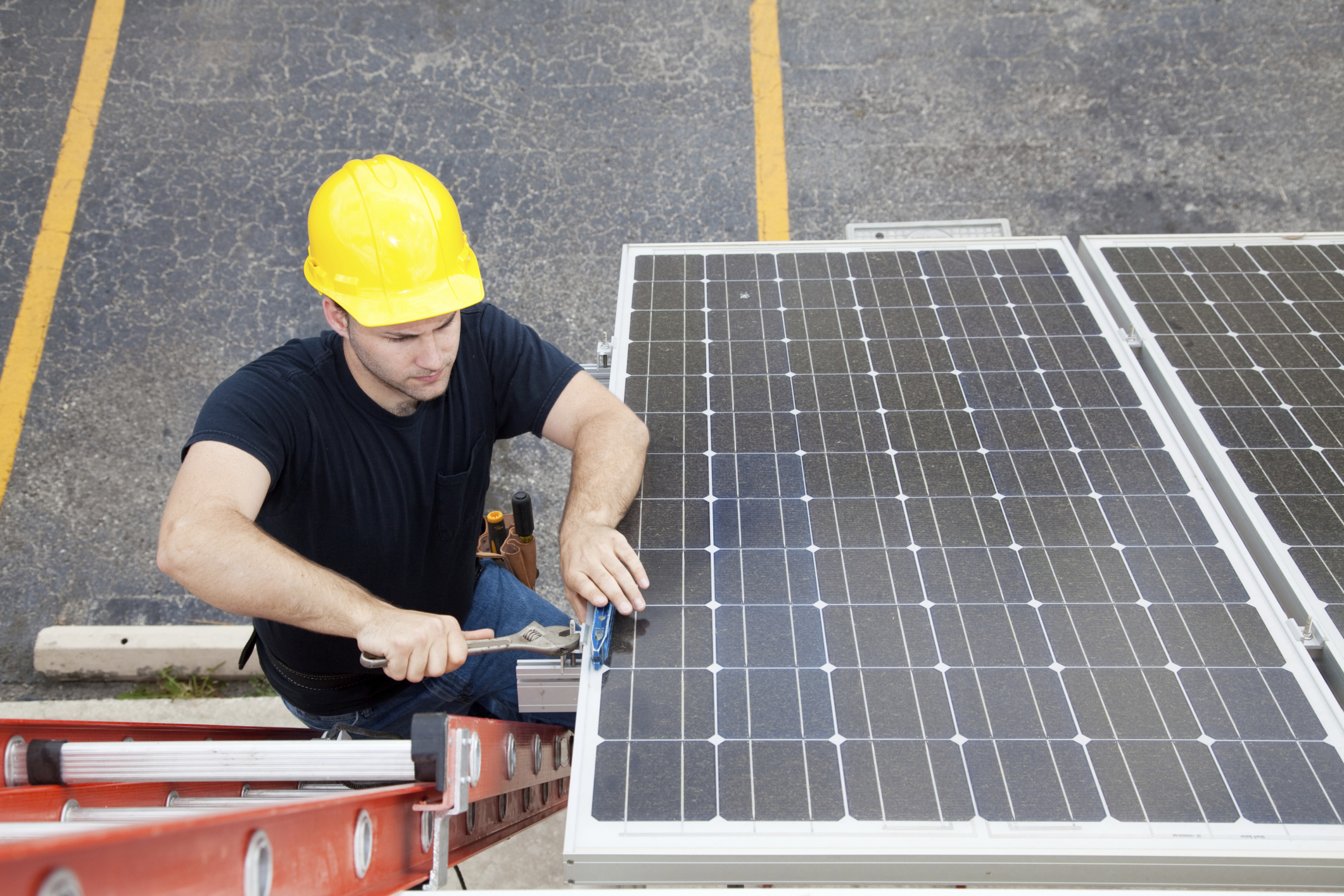 ein Mann mit Bauhelm steht auf einer Leiter und montiert eine Photovoltaikanlage