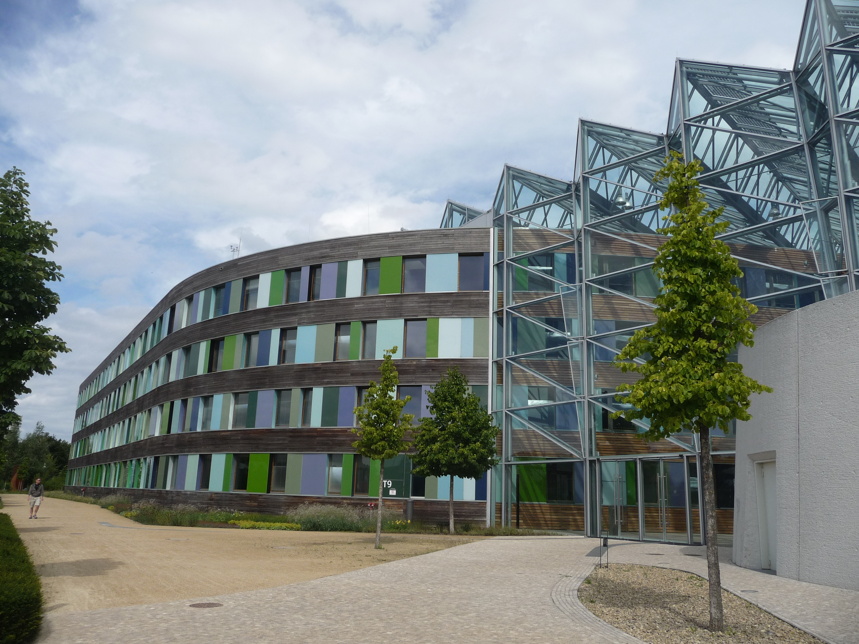 Main entrance of UBA office building in Dessau-Roßlau with glass façade. The remaining façade is made of wood, windows, and glass slabs in shades of green and blue