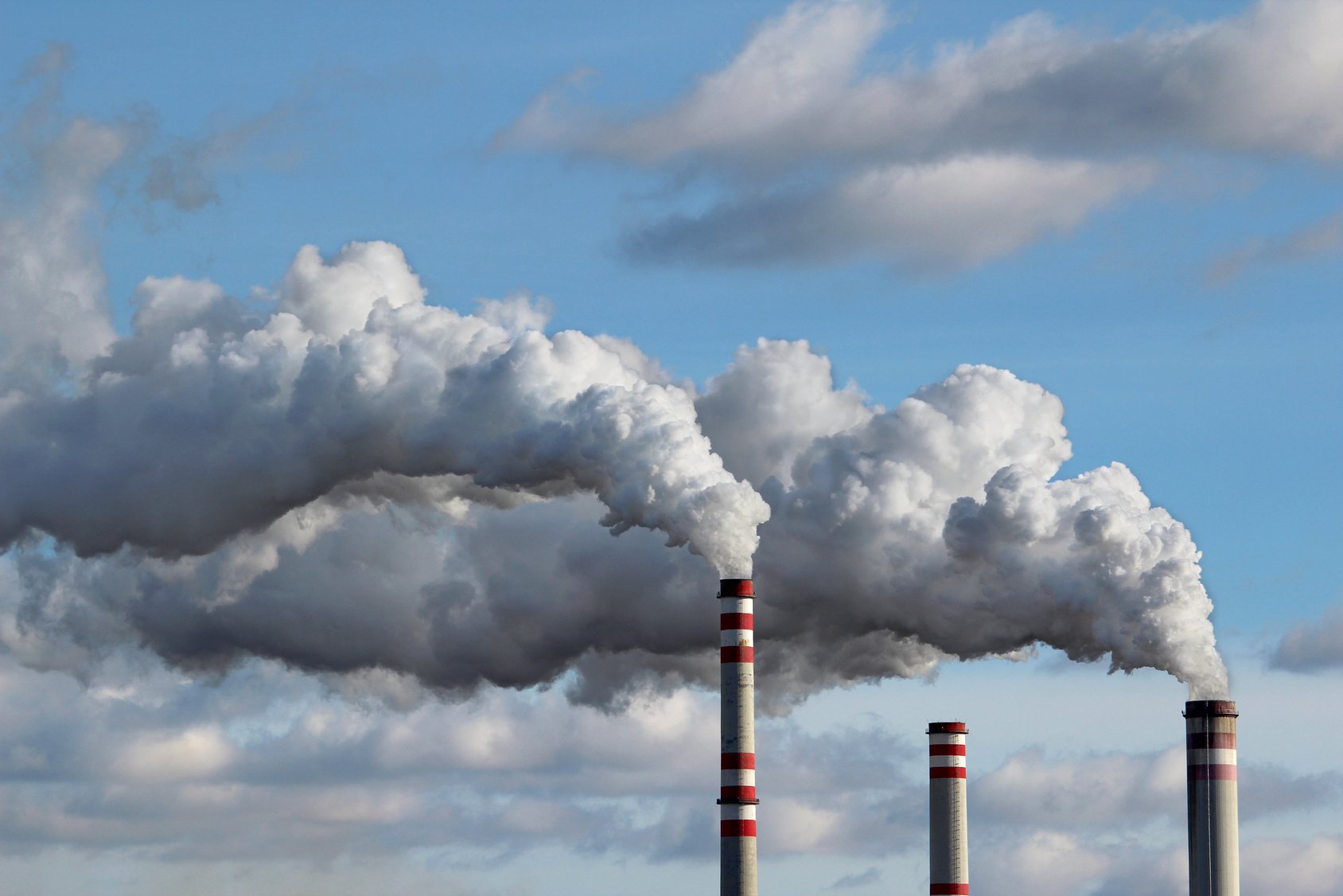 rauchende Industrie-Schornsteine vor einem bewölkten Himmel