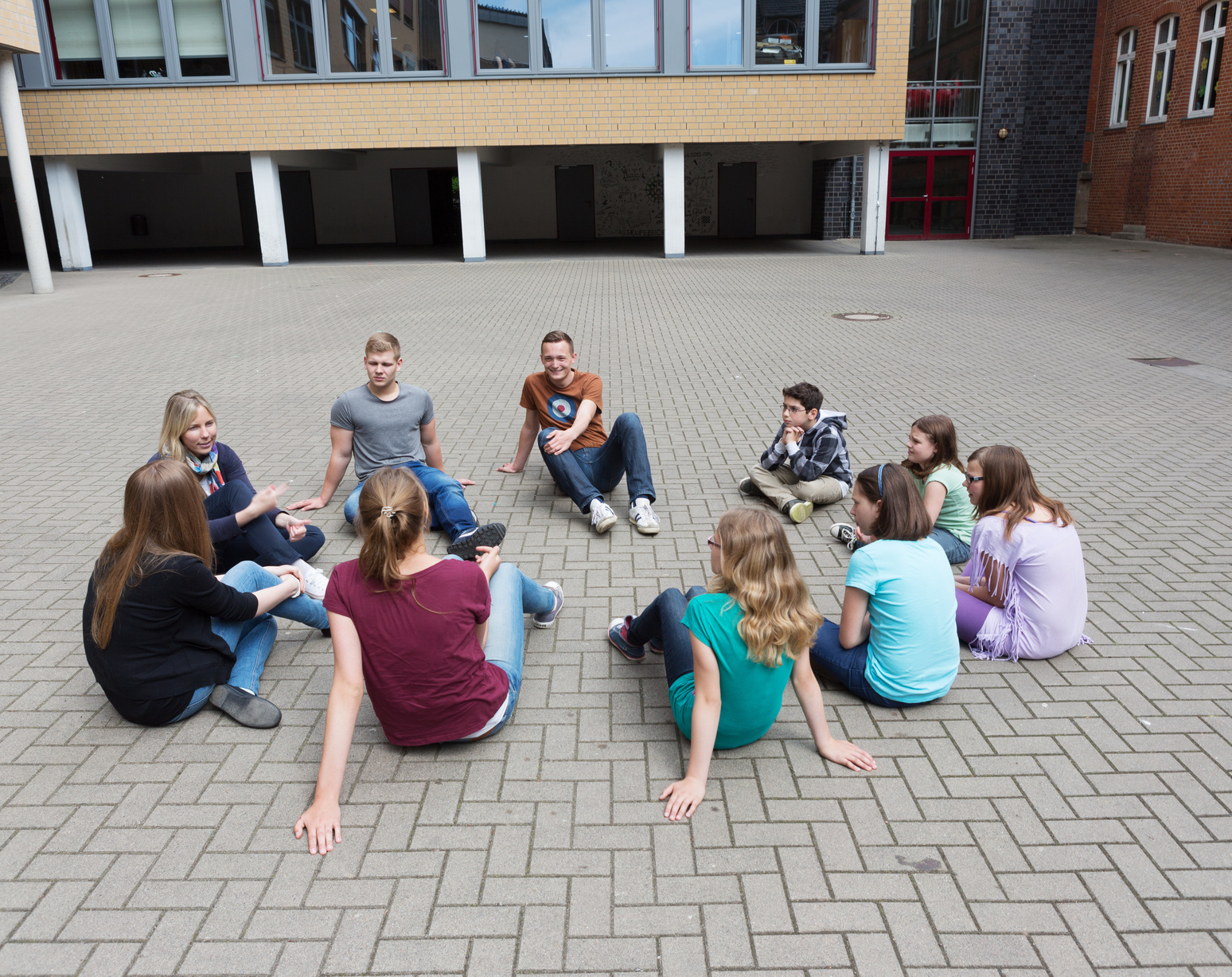 Schüler sitzen im Schulhof, der komplett mit grauen Betonsteinen zugepflastert ist