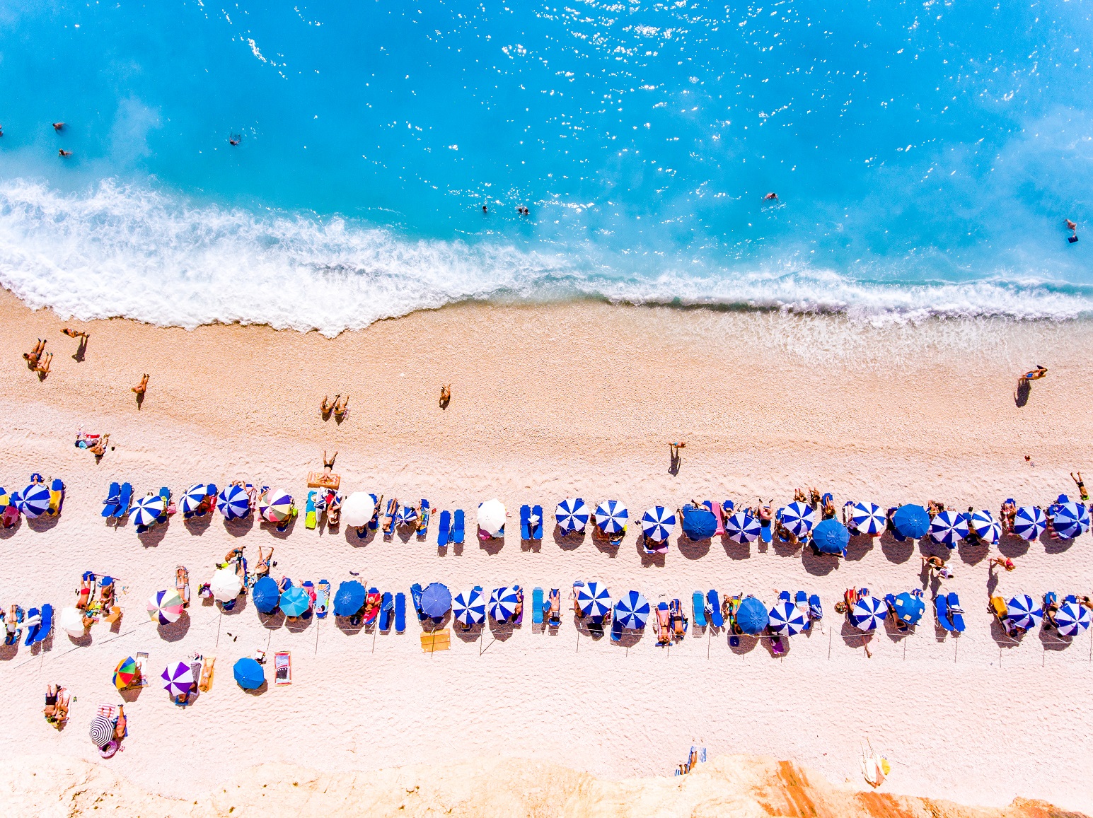 Menschen an einem Meeresstrand mit Sonnenschirmen von oben