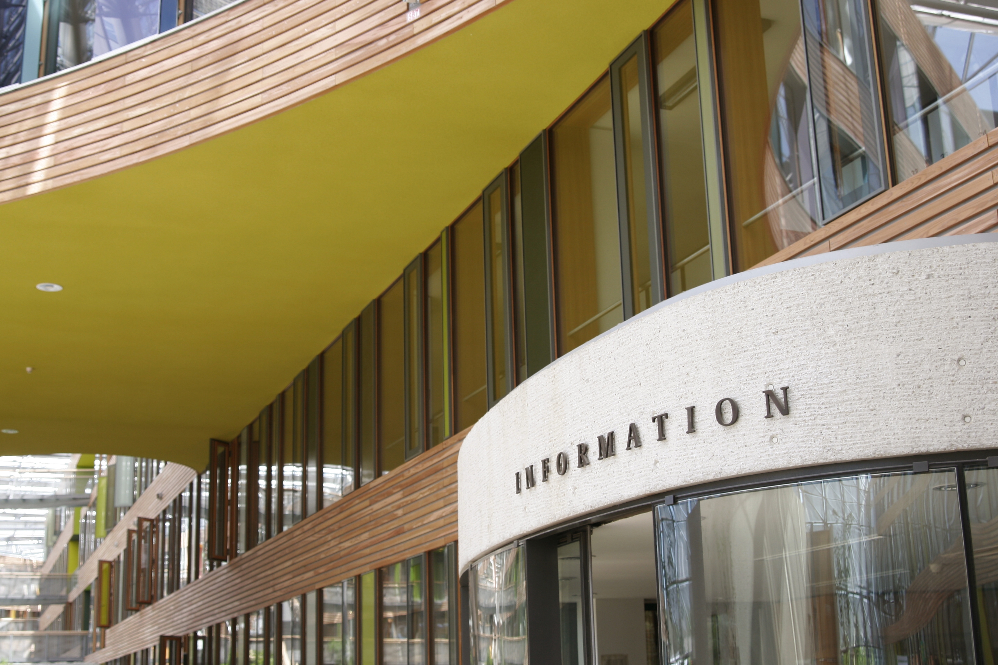 Foto im Innenhof: Moderne Innenfassade mit Glasscheiben, farbigen Flächen und Holz sowie Pförtnerloge mit der Aufschrift "Information"