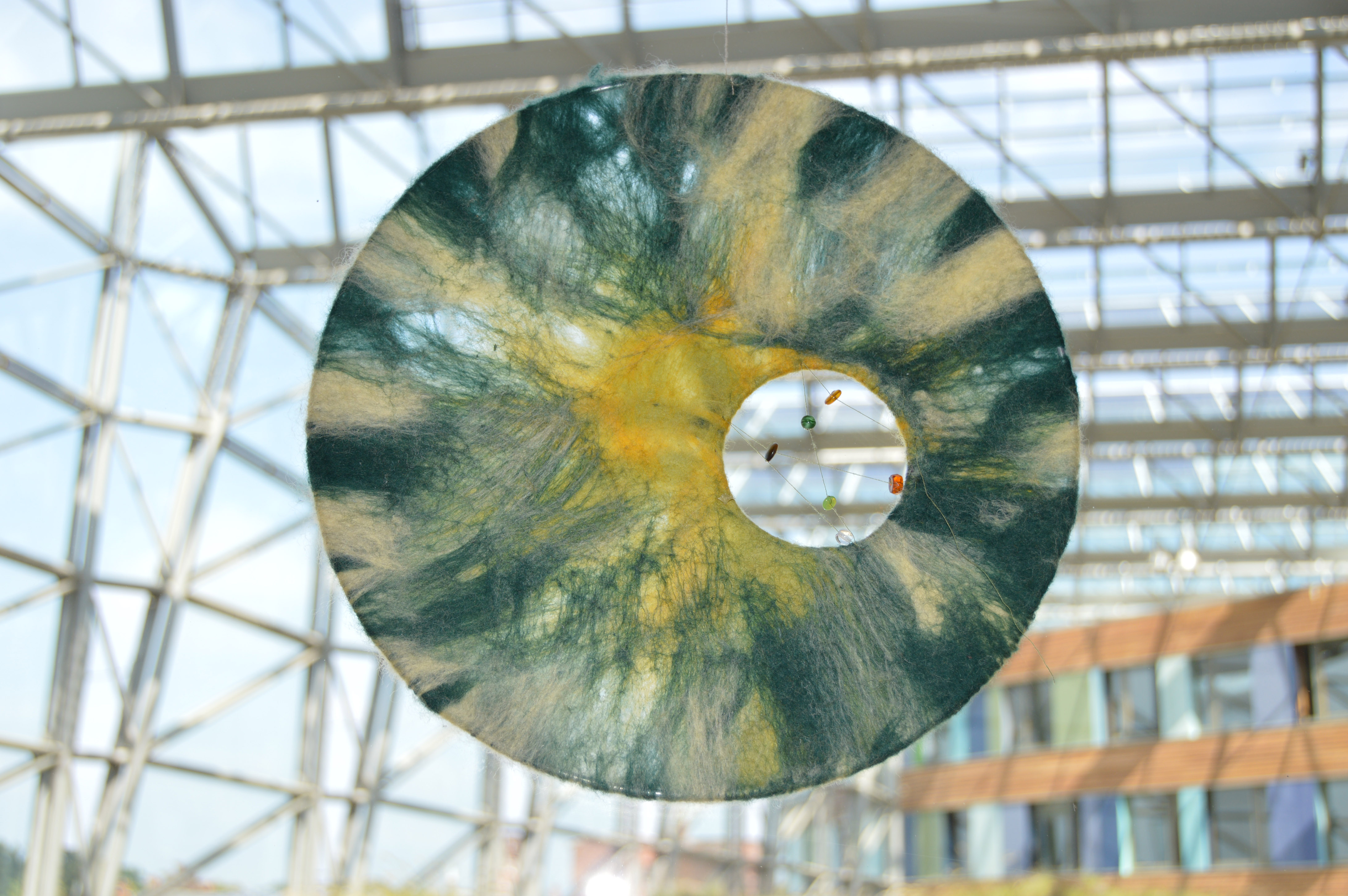 an einer Glasfront des UBA Dessau hängt eine halbtransparente Scheibe, die an Sonne, Mond, Himmel und Wolken erinnert. Ein Guckloch bietet einen Einblick ins Innere des Gebäudes
