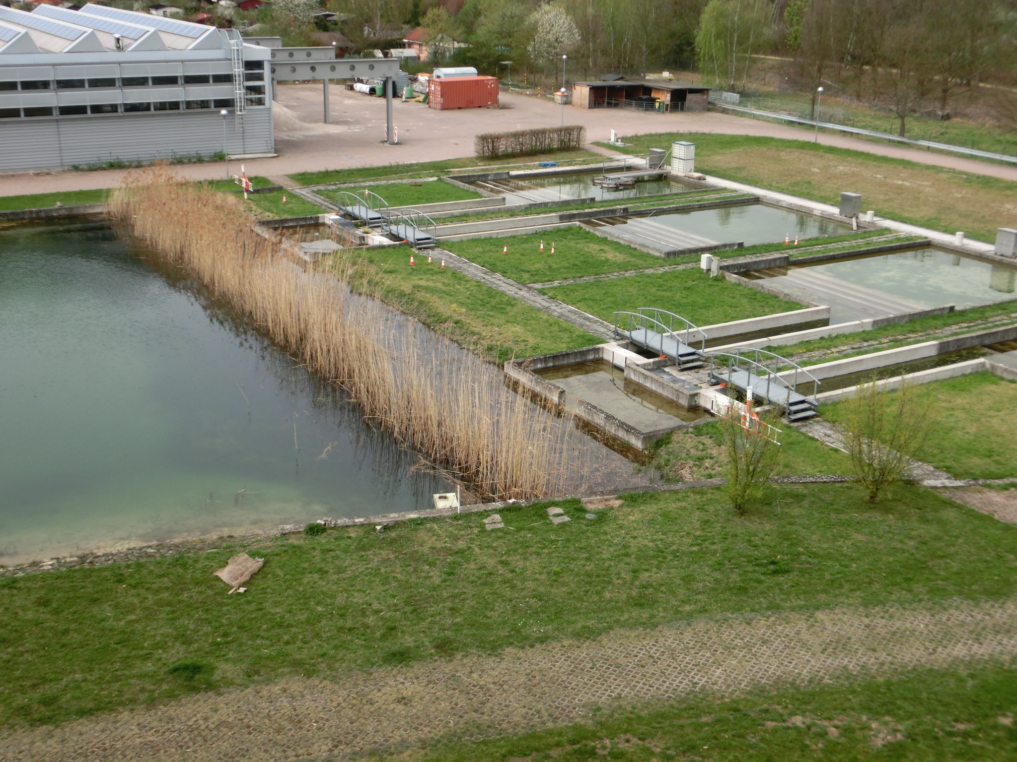 Ein größerer Teich und mehrere kleine Becken, dahinter ein Parkplatz und Gebäude