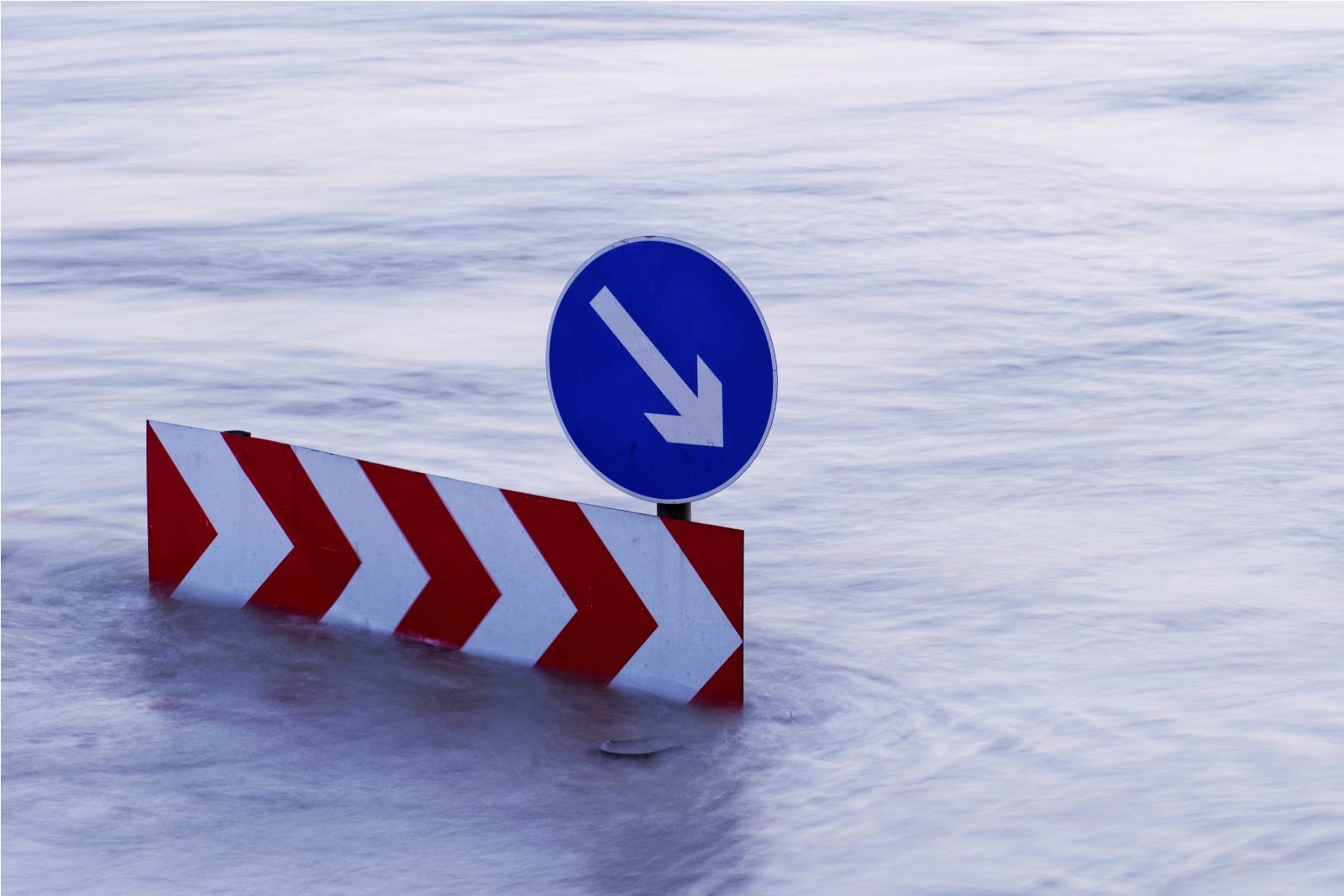 Ein Verkehsschild steht mitten im Hochwasser. Die Straße ist nicht mehr zu sehen.