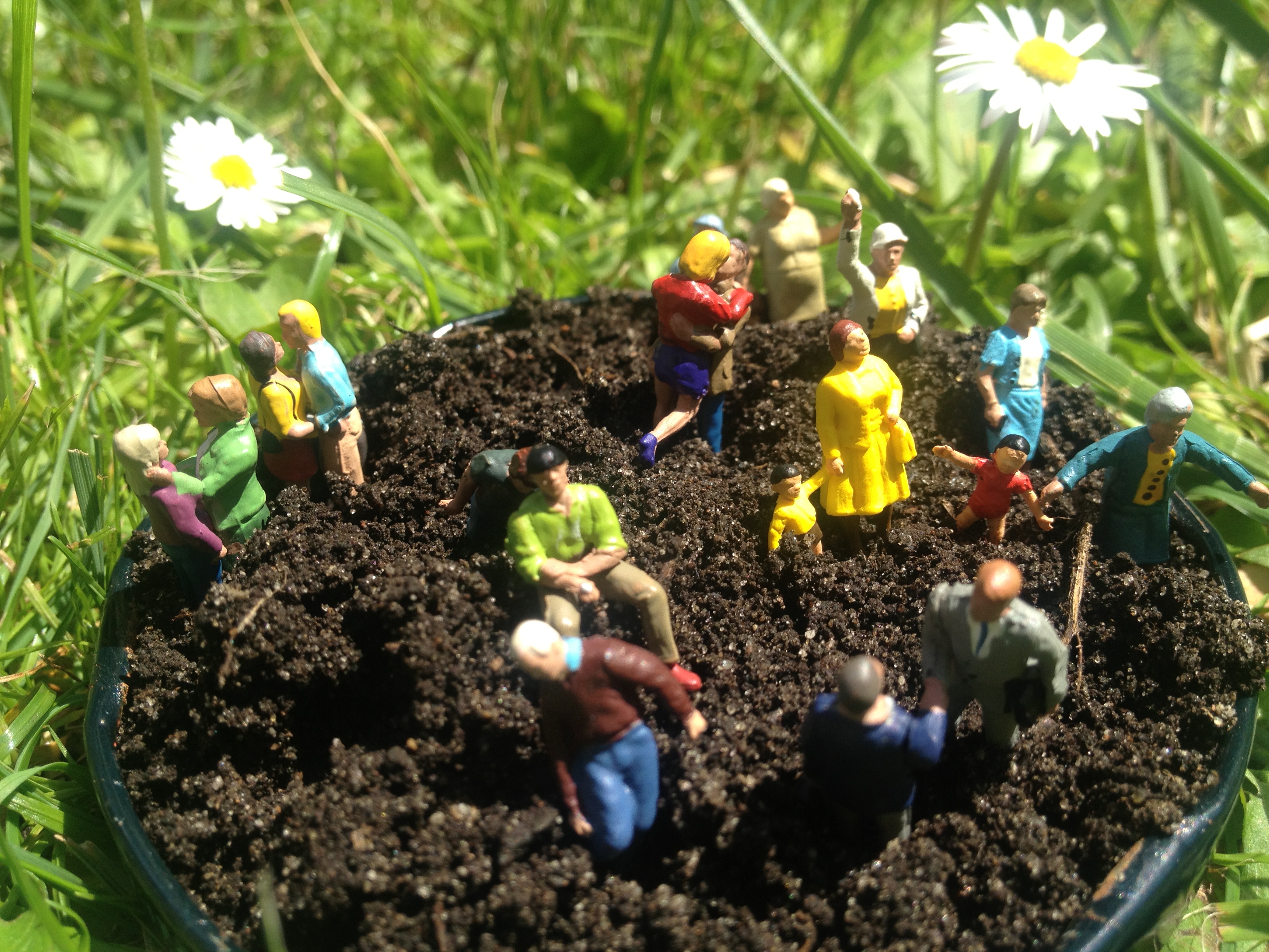 A bucket full of soil on a maedow with various toy figurines