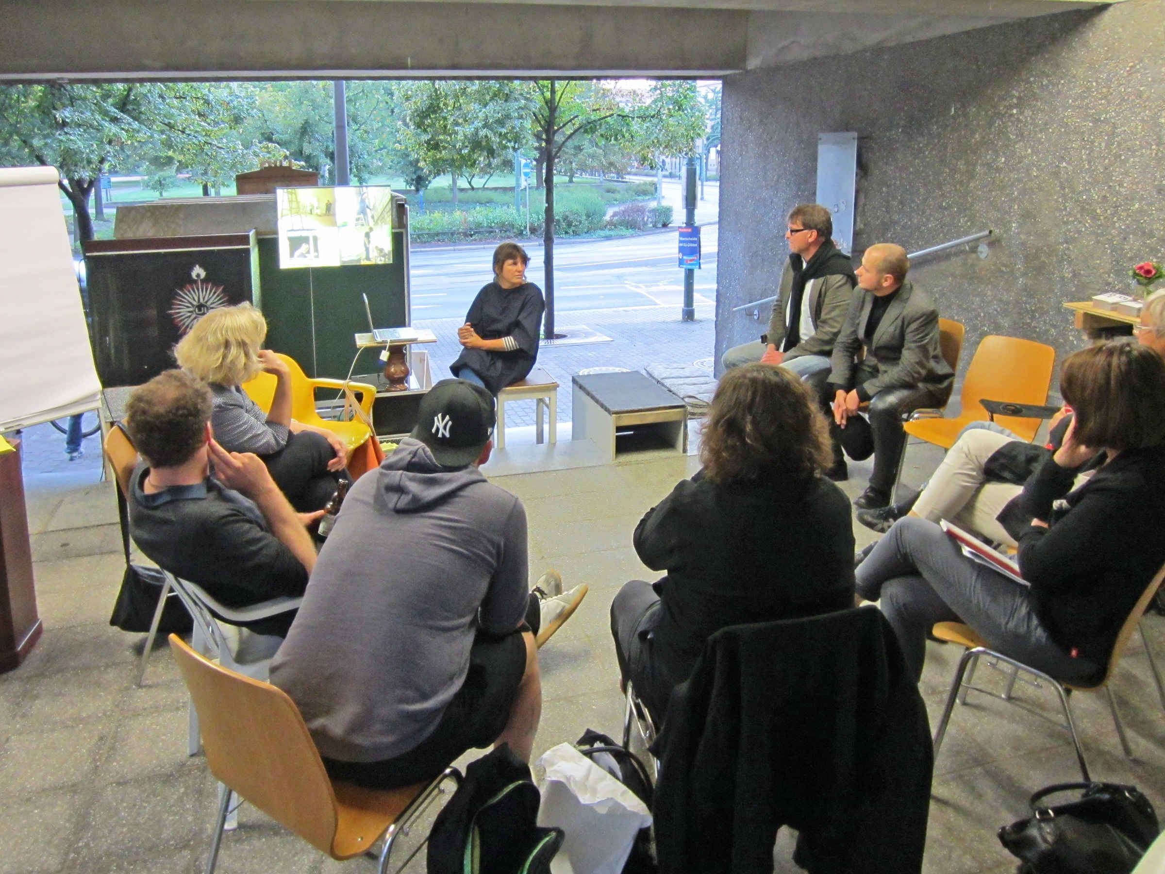 Diskussionsrunde im utopischen Institut: 9 Personen sitzen in einem Stuhlkreis