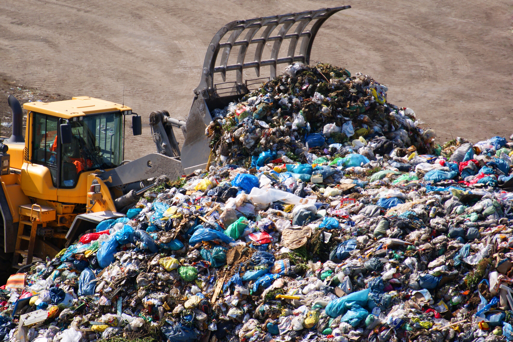 A backhoe pushes together the waste of the waste landfill