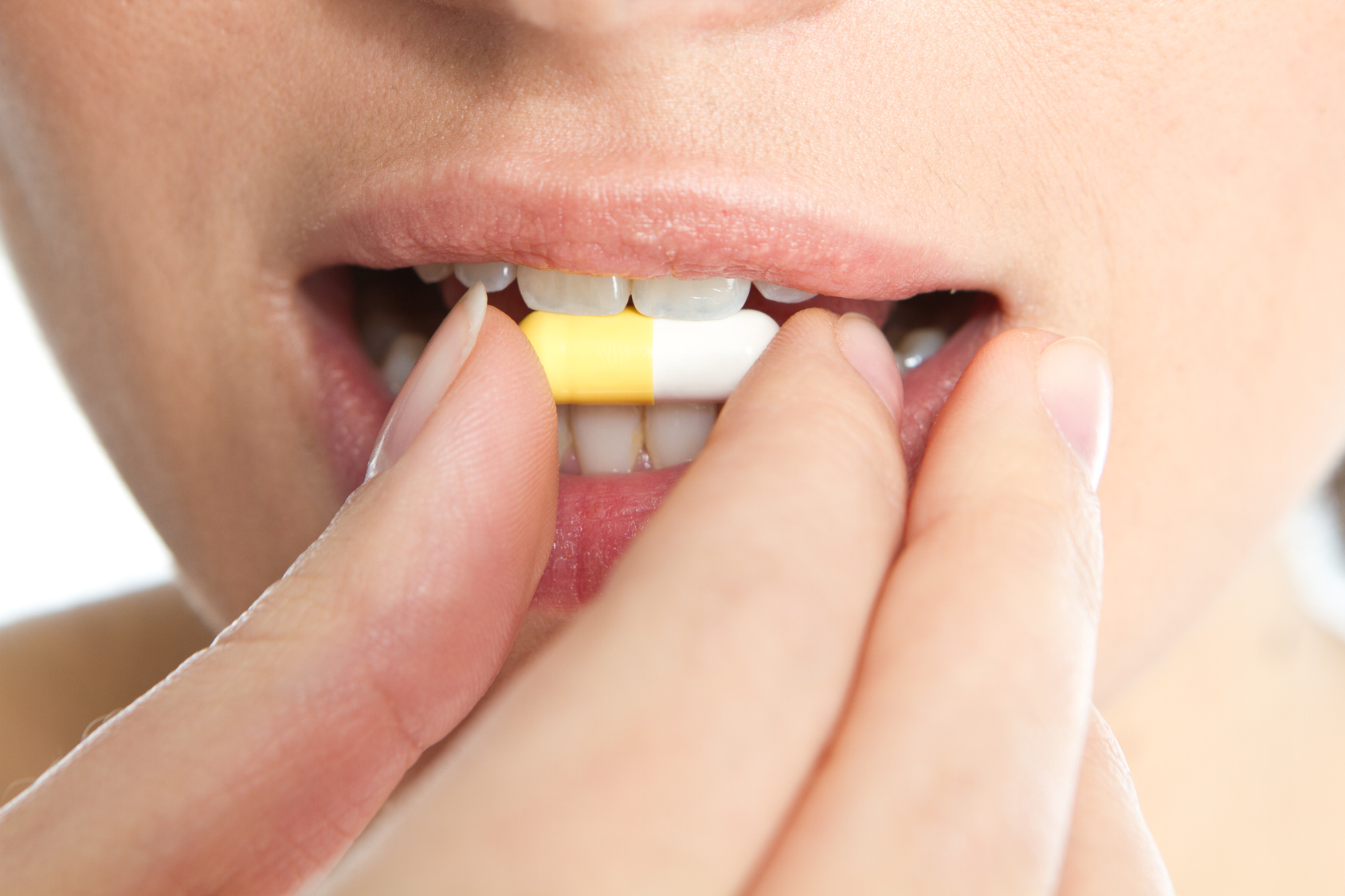 Das Bild zeigt den Mund einer Frau. Mit ihrer rechten Hand führt sie eine Tablette an ihren Mund. 