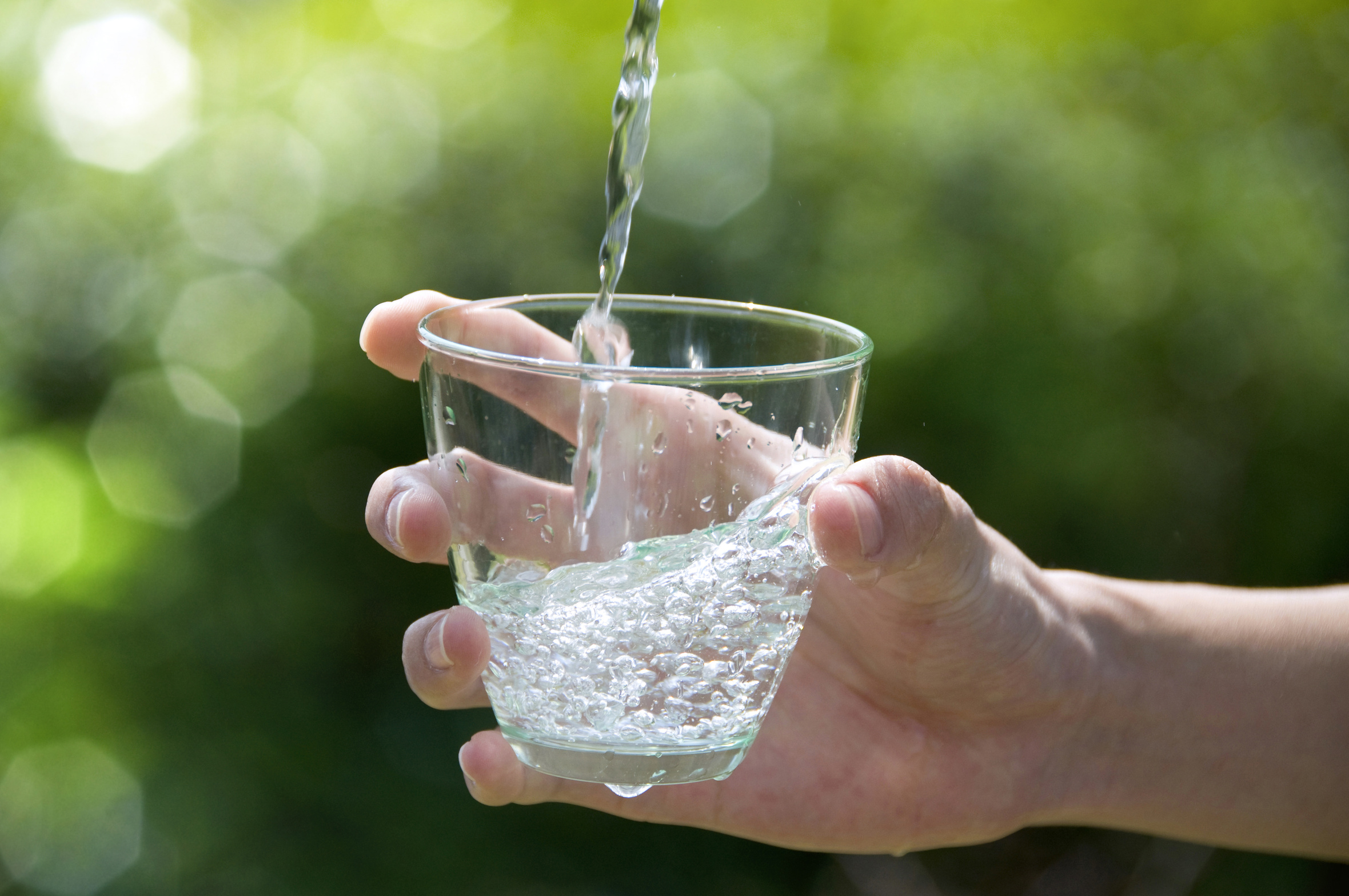 Wasserstrahl trifft von einer Hand gehaltenes Wasserglas