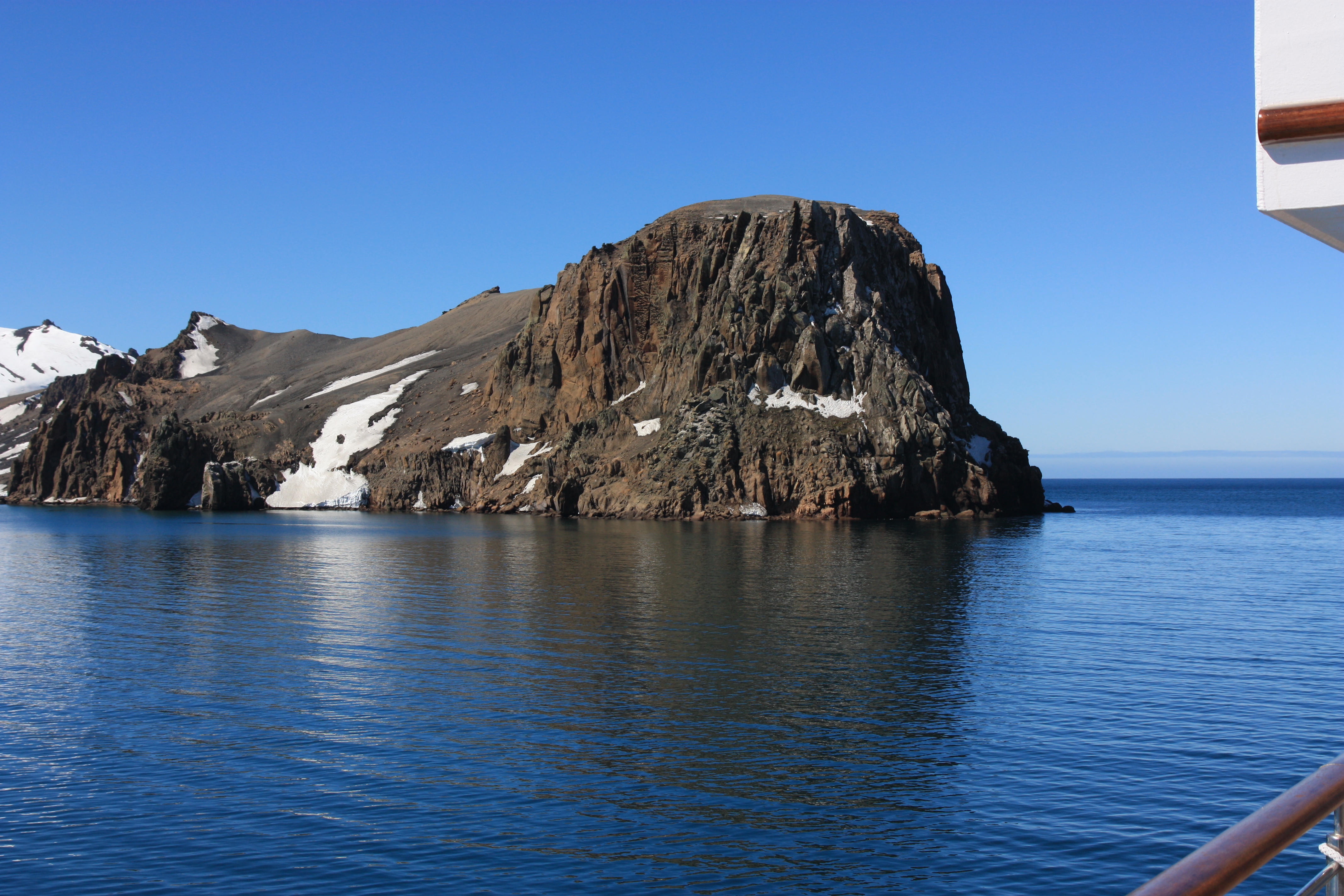 Blick von einem Schiff auf einen schroffen Berg, der aus der arktischen See ragt. 