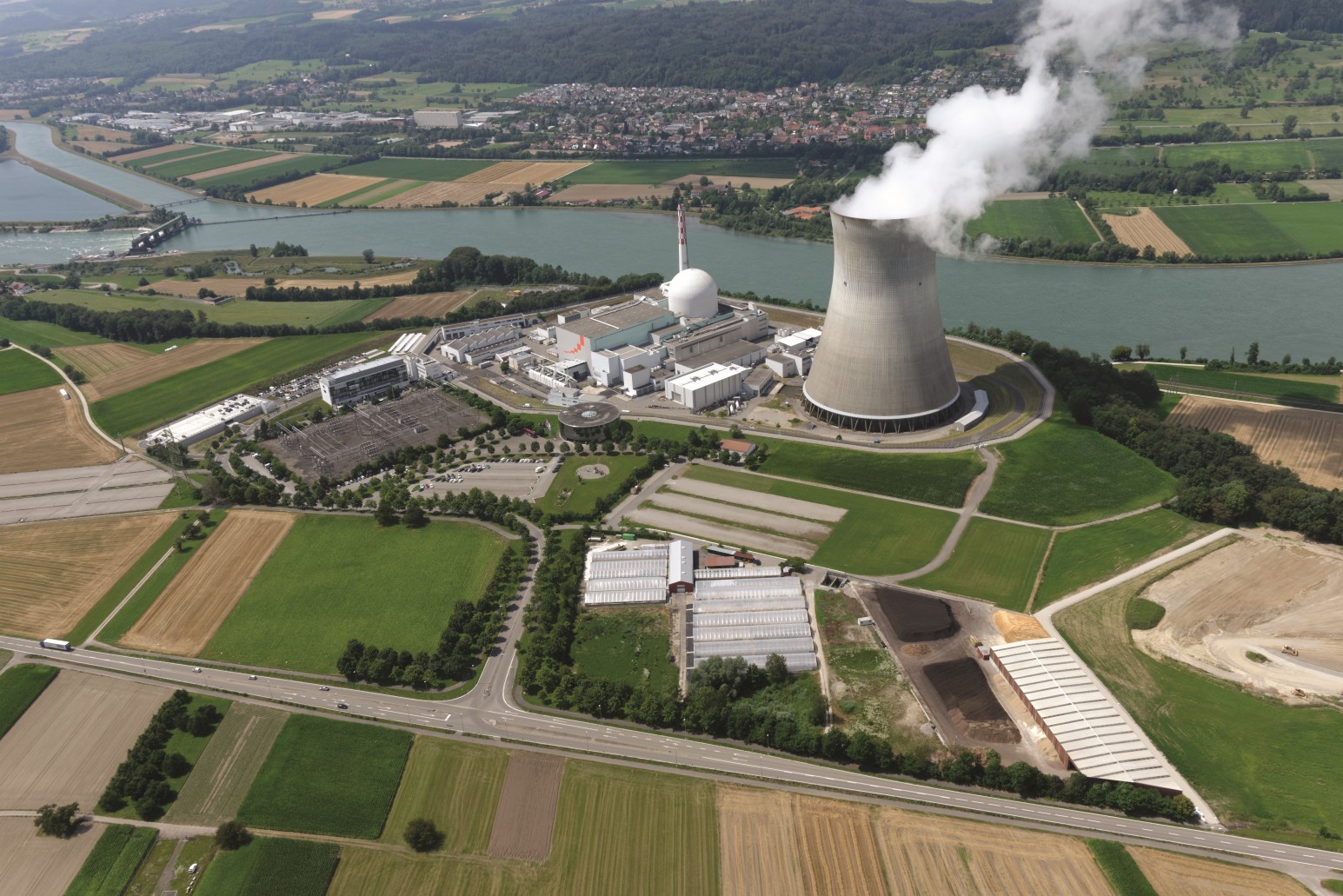 Das Bild zeigt das Luftbild eines Kernkraftwerks mit einem Wasserdampf absondernden Kühlturm am Rande eines Flusses.