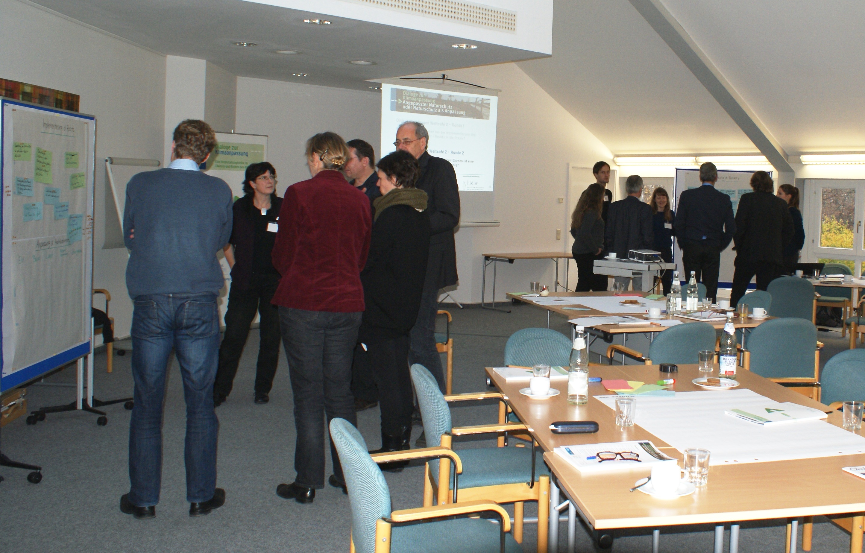 Teilnehmer stehen im Workshopraum in Grüppchen vor den Moderationswänden im Dialog miteinander.