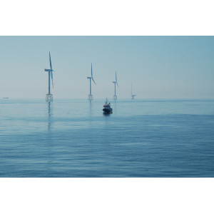 Das Foto zeigt drei Windenergieanlagen im Meer mit Jacket-Fundament (als Fachwerk konstruierte Gründungsstruktur). Ganz im Hintergrund ist die Forschungsplattform FINO1 sichtbar. Im Vordergrund ist ein im Verhältnis zu den Windenergieanlagen klein wirkendes Schiff sichtbar.