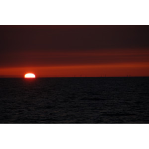 Das Foto zeigt einen Sonnenuntergang über dem Meer. Am Horizont sind bei dem Windenergieanlagen zu sehen.