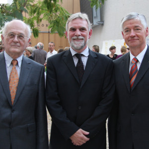 drei Männer im Anzug stehen in einer Reihe aufgestellt im UBA-Gebäude Dessau und schauen in die Kamera