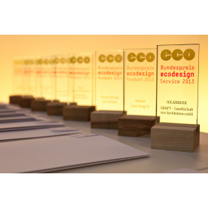 Auf einem Tisch stehen in einer Reihe die Sieger-Trophäen aus Glas mit dem Logo des Bundespreis Ecodesign und dem Namen des jeweiligen Preisträgers