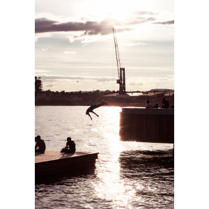 Im Hafen von Oslo: Bei untergehender Sonne springt ein Mann von einem Steg ins Wasser, davor sieht man zwei Personen, die in der Abendsonne sitzen.