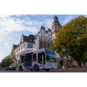 Ein mit Wasserstoff betriebener Kleinbus steht auf der Straße vor einem alten Gebäude und einem Baum