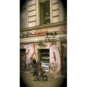 Ein Mann spielt aus dem Fenster seiner Wohnung heraus Trompete, auf dem Bürgersteig darunter schaut ein kleiner Junge mit seinem Fahrrad hoch zu dem Mann im ersten Stock und hört ihm zu.