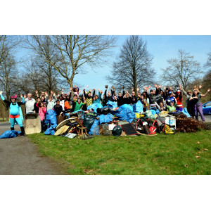 Gruppenfoto von etwa 30 Personen nach einer Müllsammelaktion im Wald und freien Feld. Einige Personen sind verkleidet, im Vordergrund liegt der gesammelte Müll.