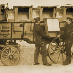 Zwei Arbeiter laden eine Tonne auf einen Wagen