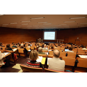Veranstaltungsambiente im Hörsaal des Umwelbundesamtes: Der Blick geht noch vorne auf das Podium. Auf dem Podium präsentiert eine Teilnehmerin einen Vortrag , der auf der Projektsfläche über dem Podium abgebildet wird.